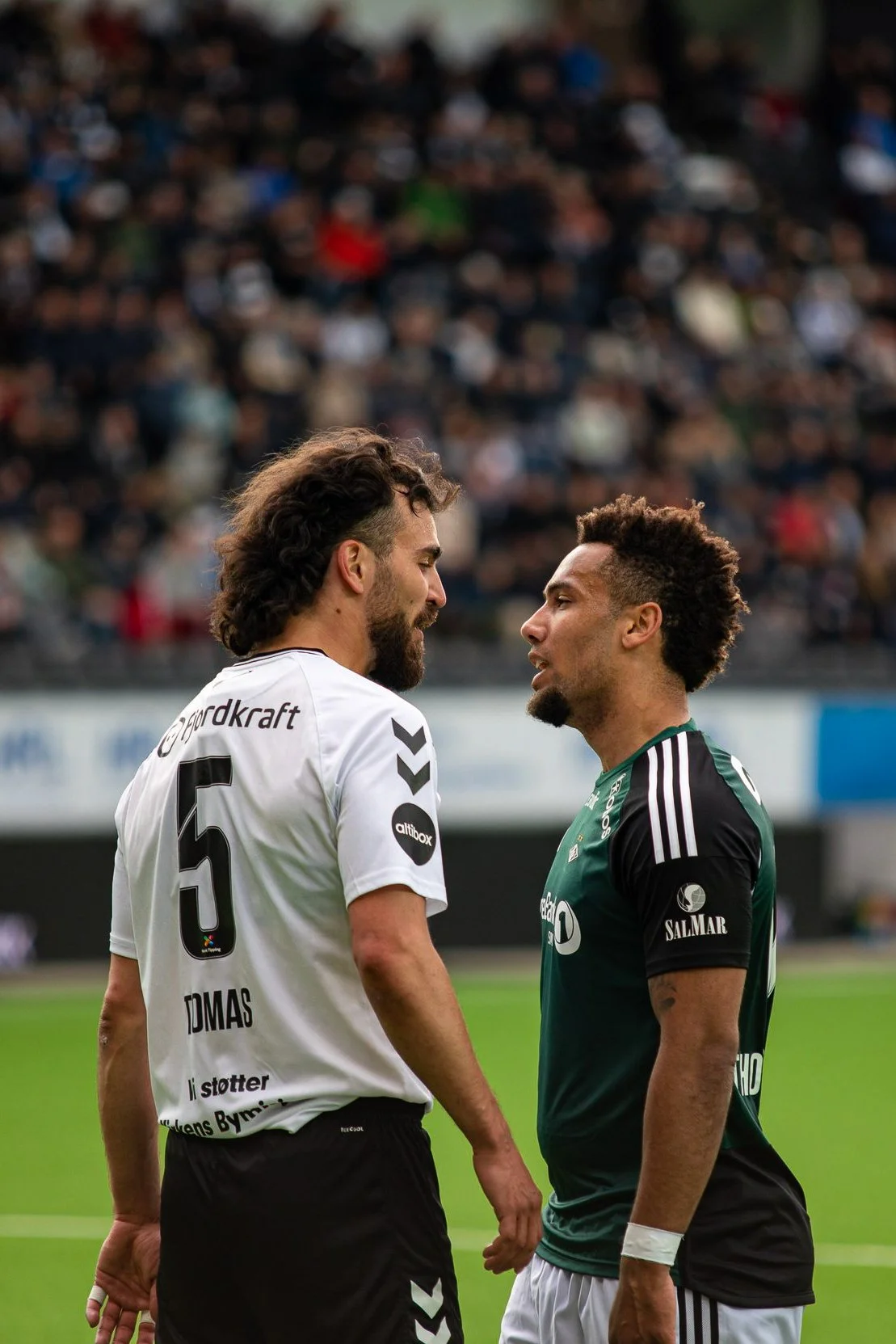 Two soccer players face each other on the field during a game, surrounded by a blurred crowd in the stands.