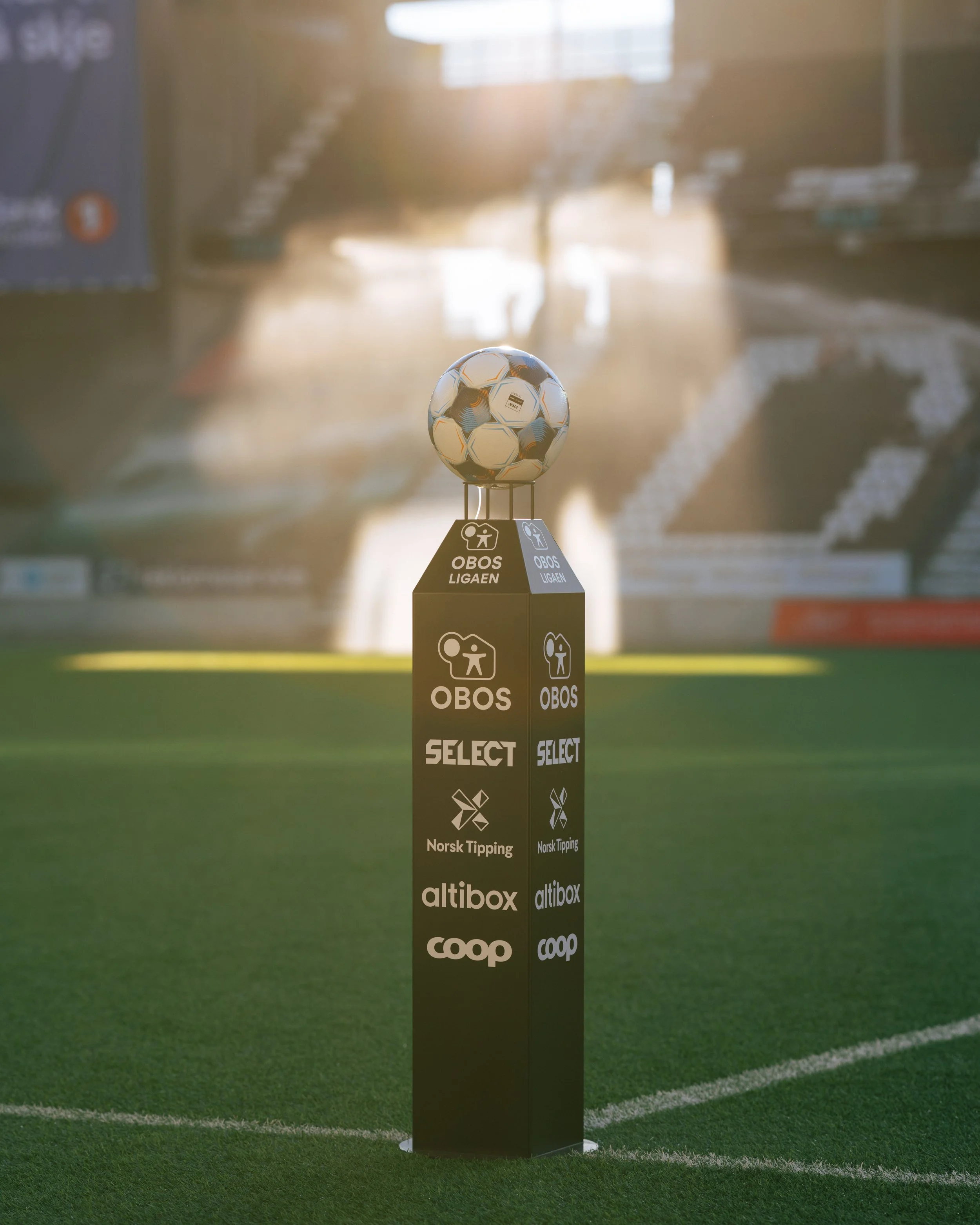 A soccer ball on a pedestal in the middle of a stadium, with sunlight shining behind.