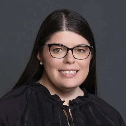 A woman with long dark hair, glasses, and pearl earrings smiling at the camera.