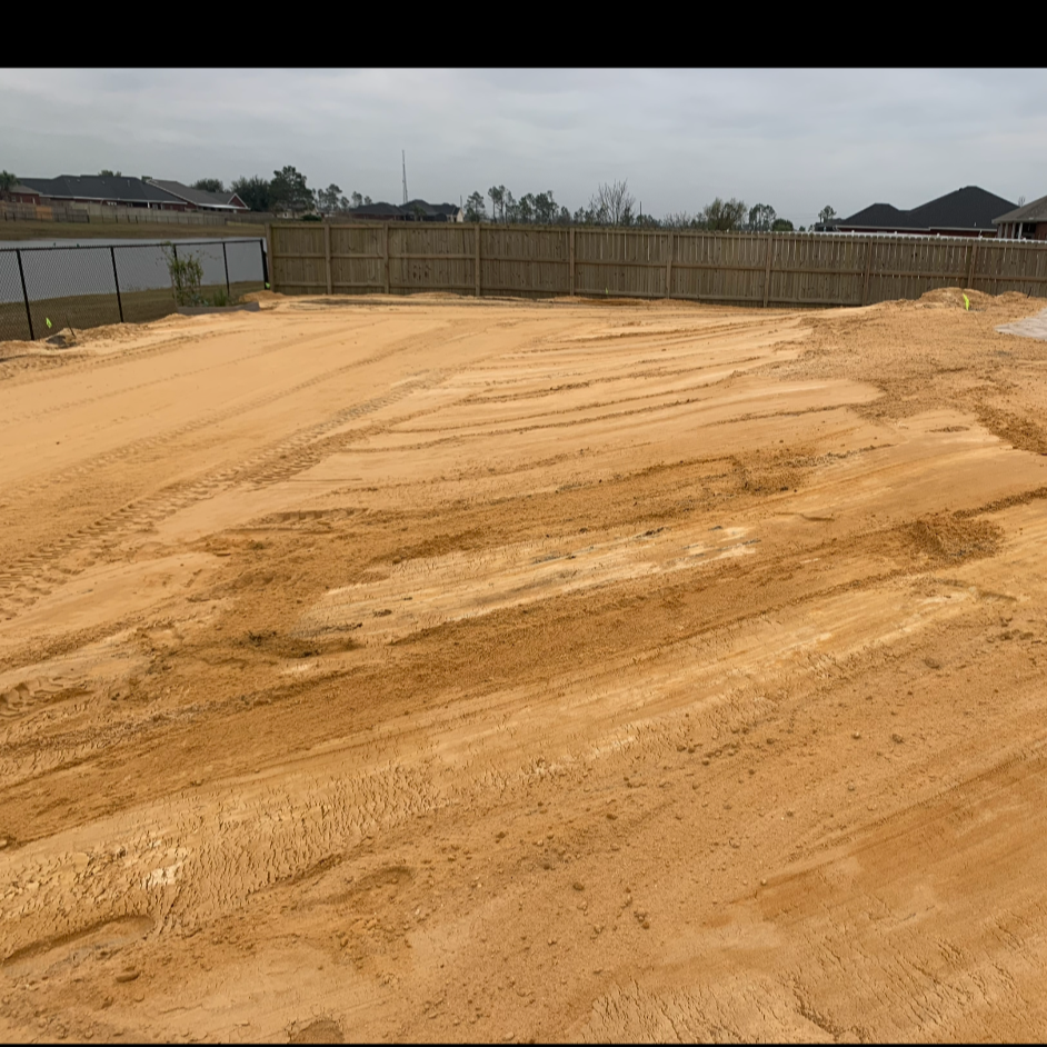A dirt backyard under construction with tire tracks and a new wooden fence surrounding the area.