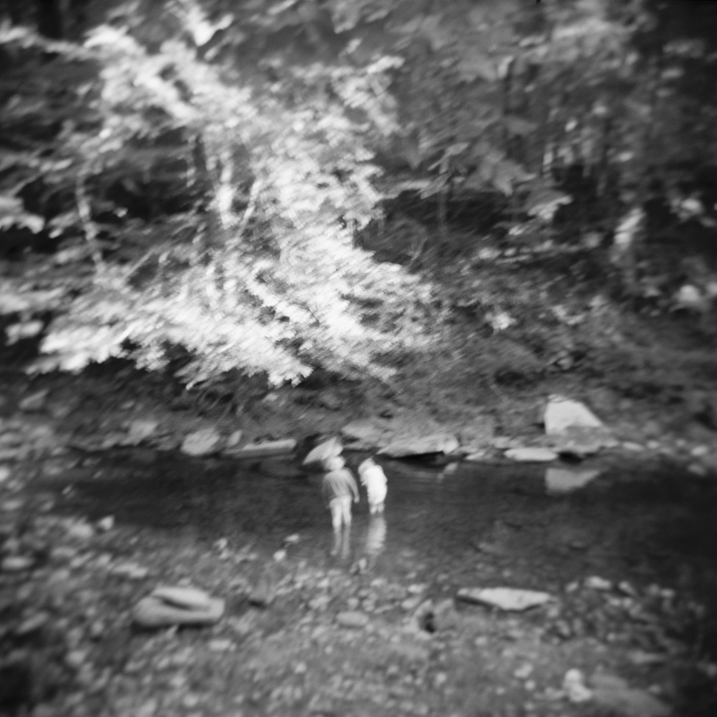 Two people standing in a stream at night surrounded by trees and rocks.