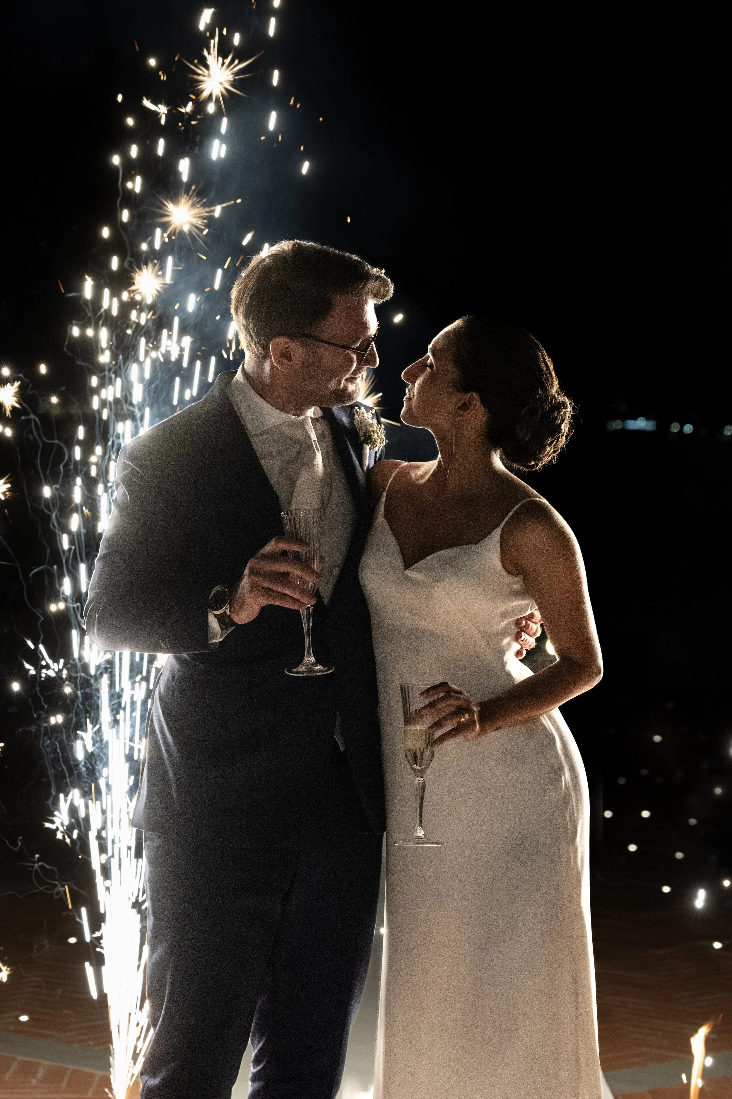 A couple in wedding attire celebrating with sparklers and champagne on a night of celebration.