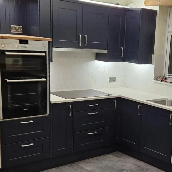 Kitchen with dark blue cabinets, white countertops, built-in oven, electric stove, and a white backsplash. There's a window on the right side.