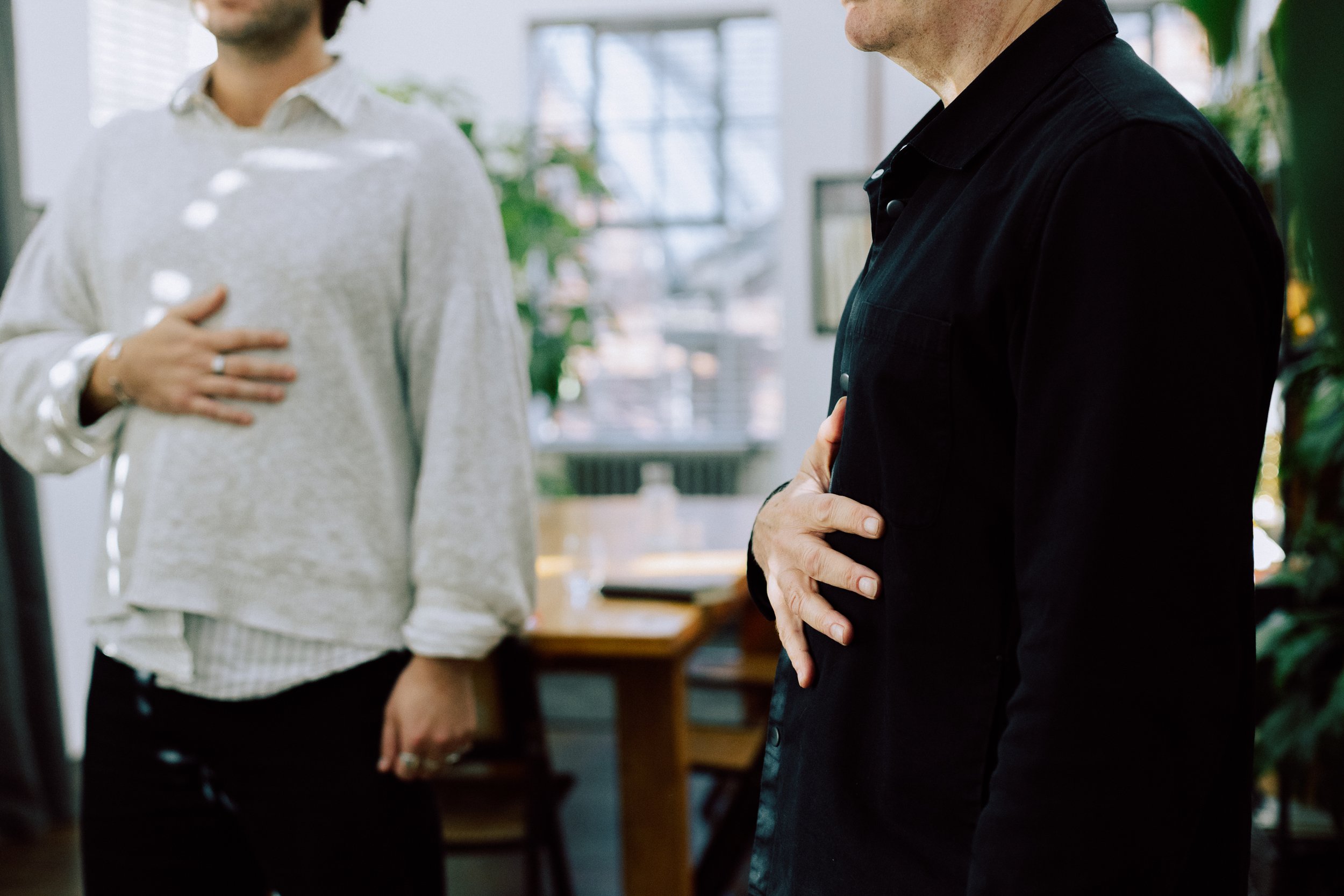 Two people standing indoors, each with one hand over their chest, possibly taking an oath or making a pledge.