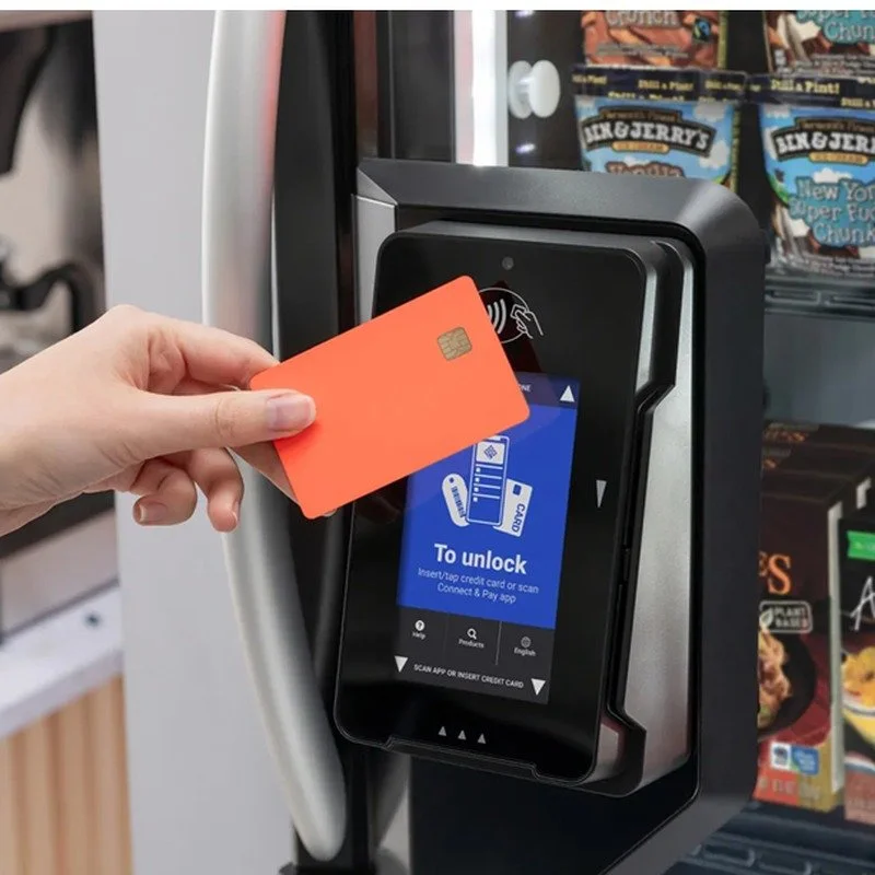 A person holding a red credit card in front of an electronic payment terminal at a vending machine.