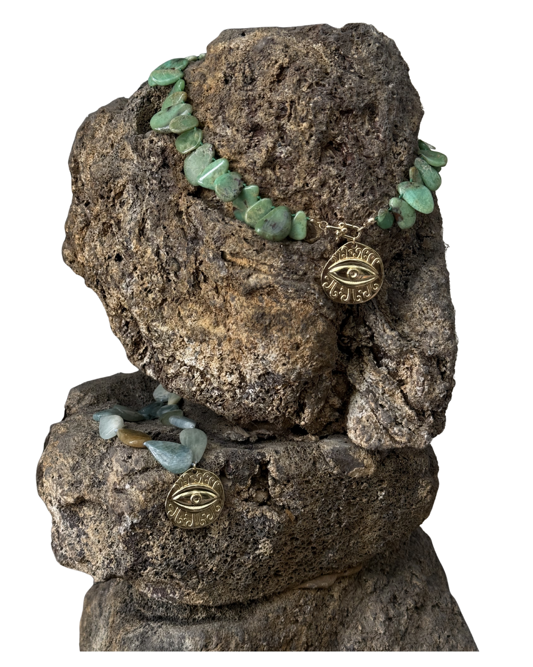 Ein Schmuckstück auf zwei Steinen, bestehend aus einer Kette mit grünen Steinen und einem Anhänger mit einem Auge-Design sowie Ohrringen mit ähnlichen Anhängern.