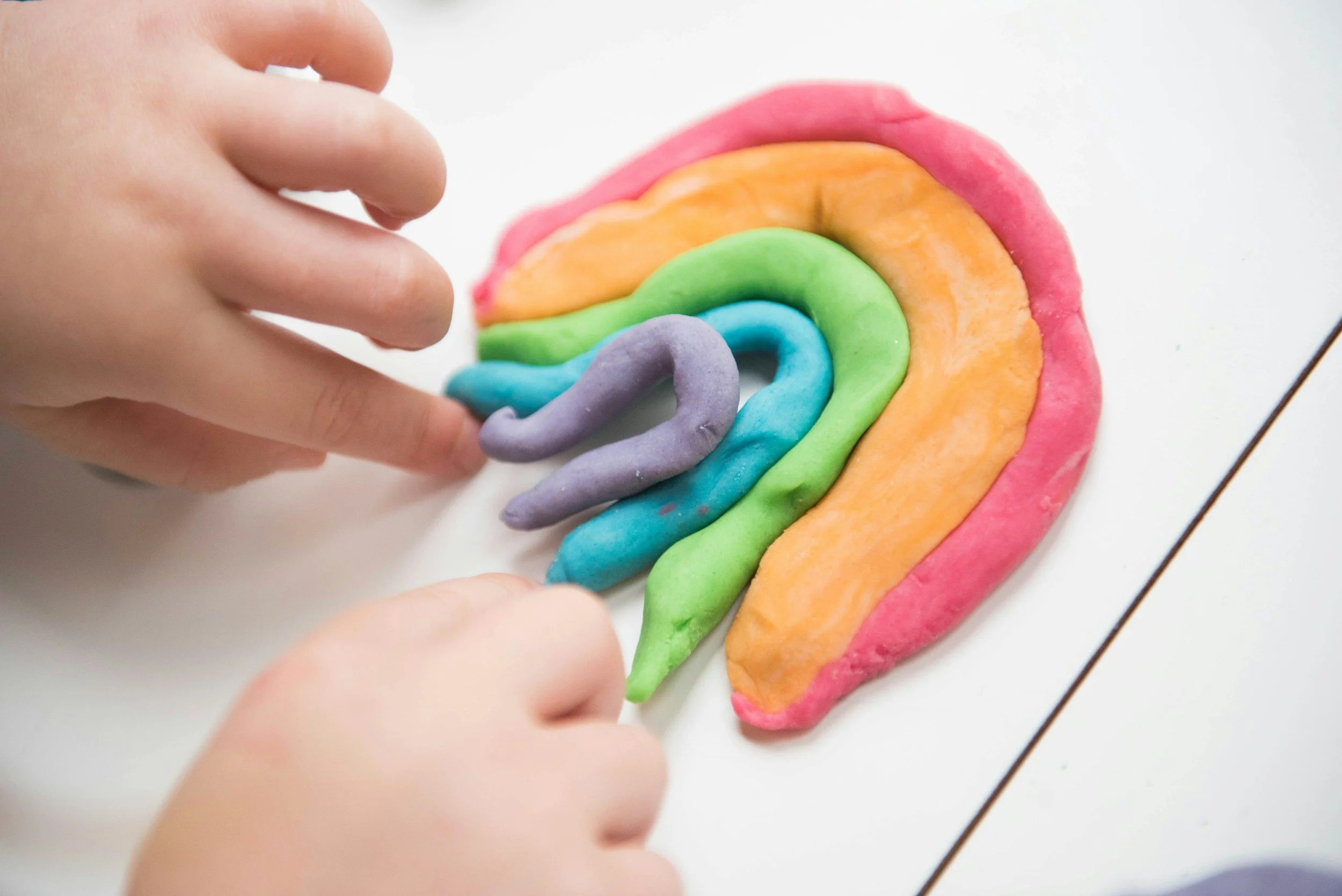 Child's hands decorating a rainbow-shaped cookie with colorful fondant or icing.