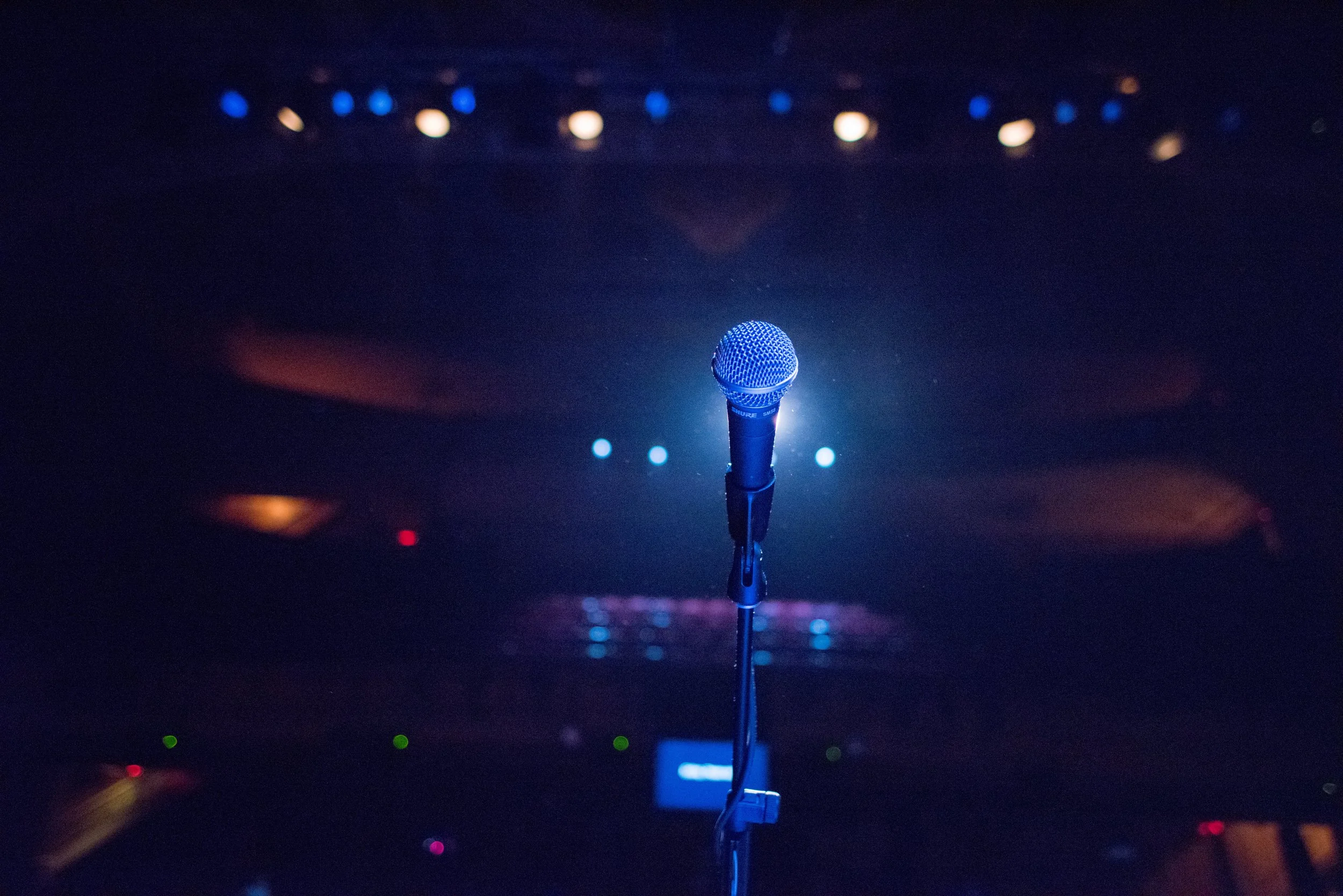 A microphone on a stand on a stage, with stage lights and a dark background, ready for a performance or speech.