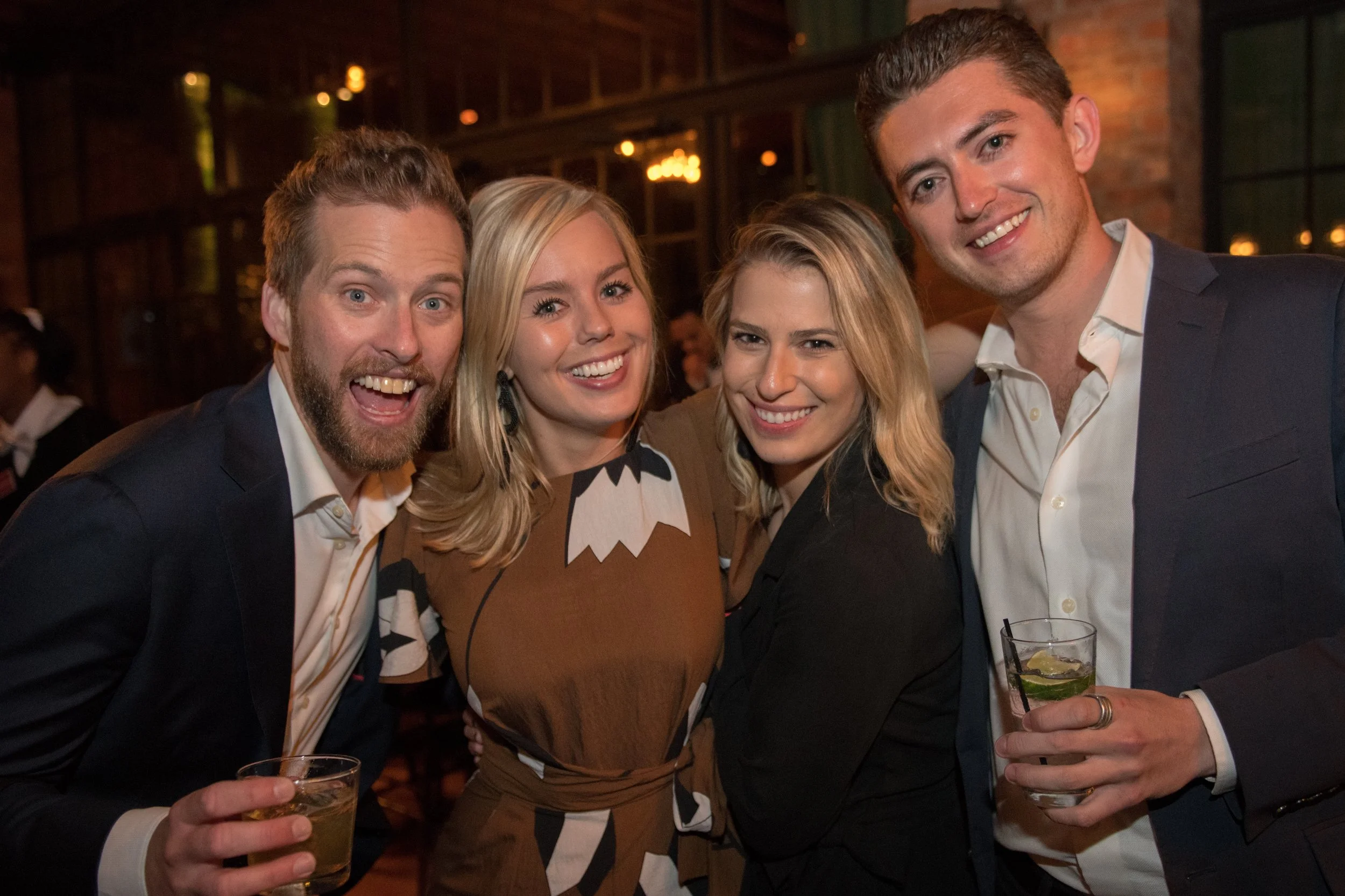 Group of four friends smiling and enjoying drinks at a social gathering or party