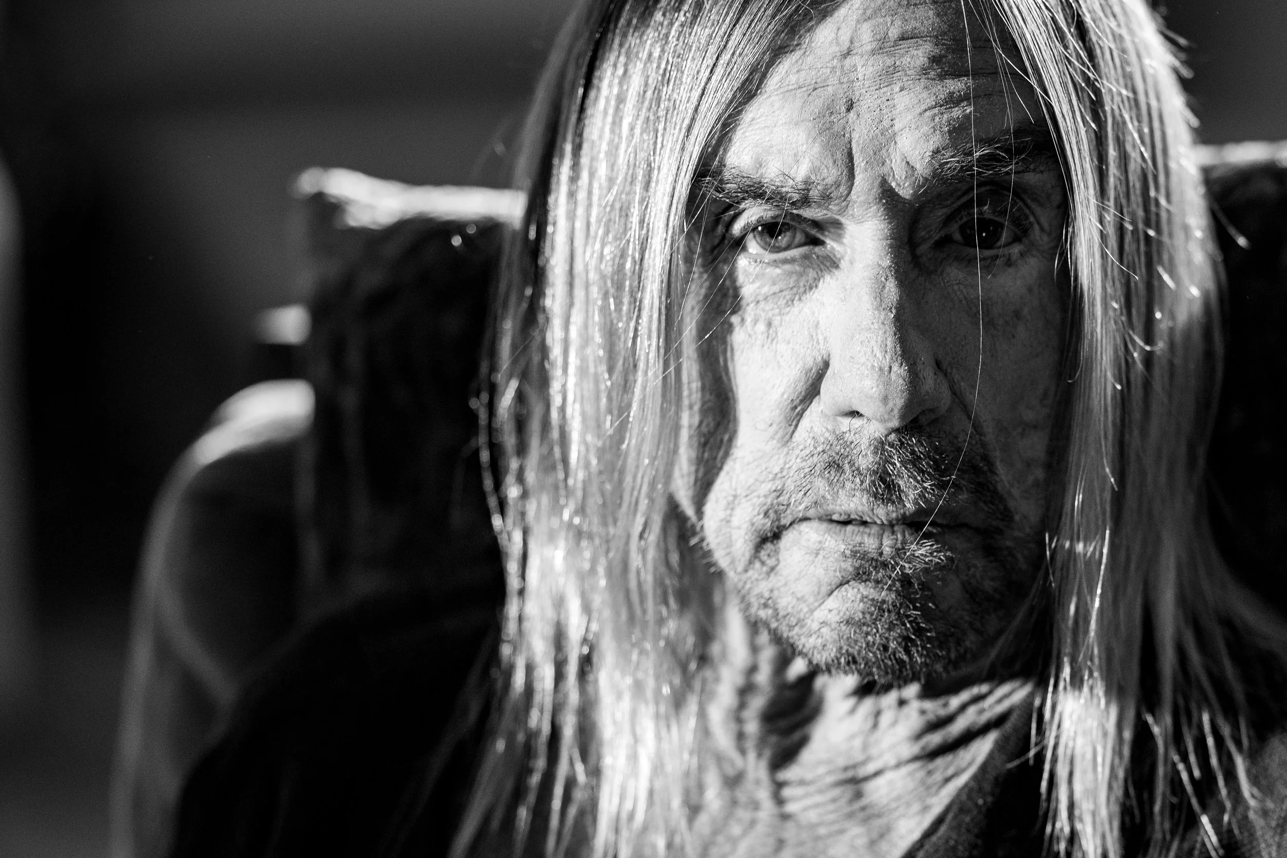 Close-up black and white portrait of a man with long hair, staring intensely into the camera, with a serious expression.