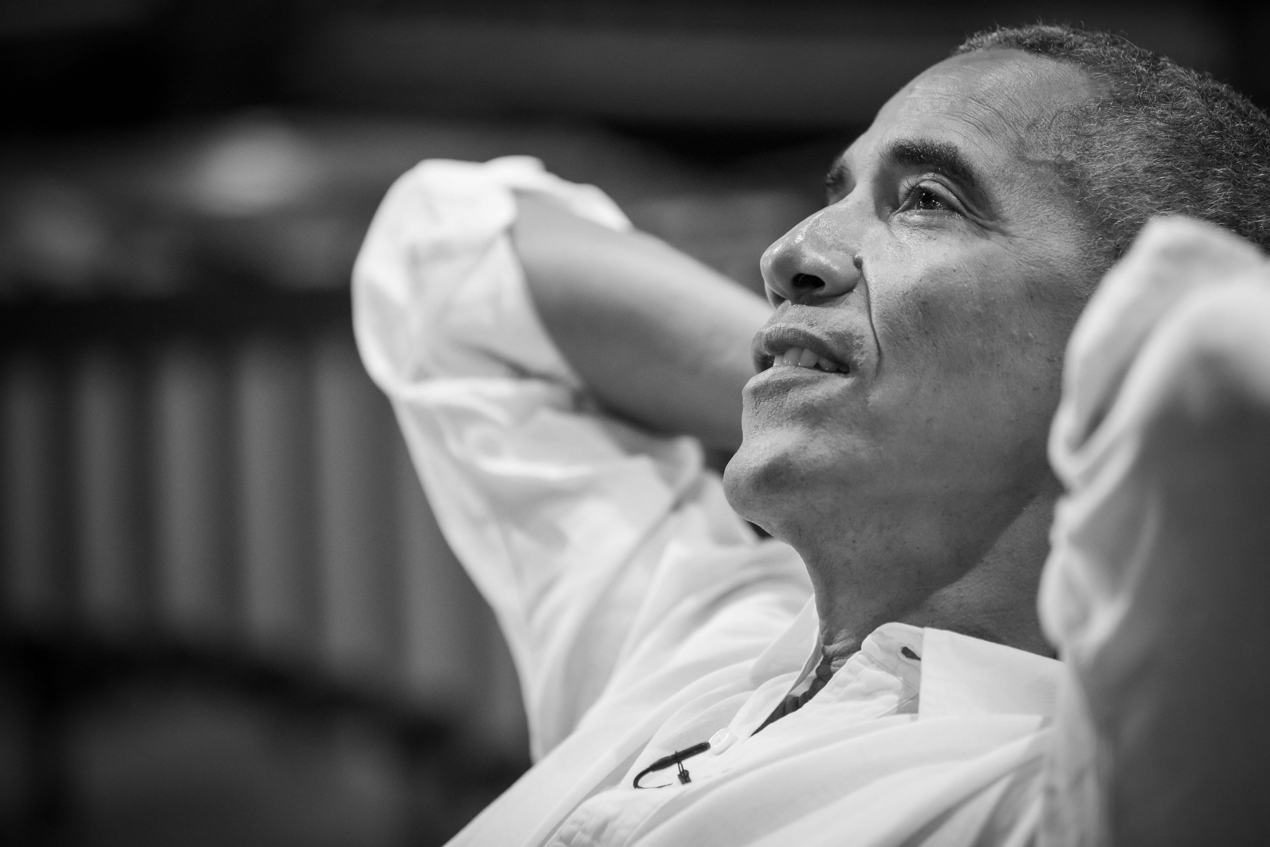 A middle-aged man with short curly hair, wearing a white shirt, is looking up with a thoughtful expression inside a room with a blurred background.