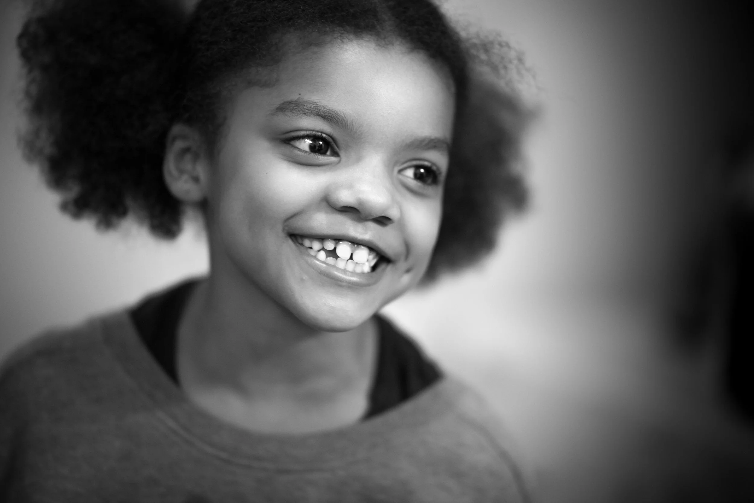 A smiling young girl with curly hair shows her teeth, looking joyful and happy.