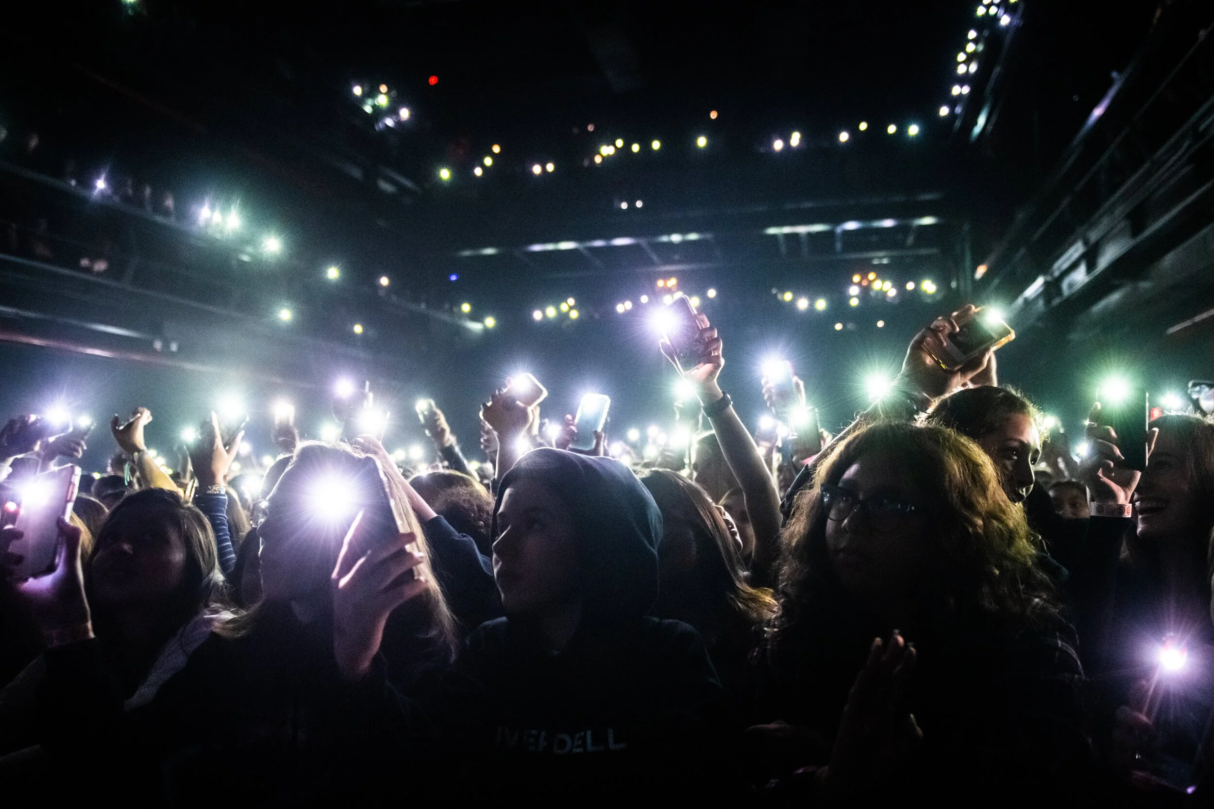 Crowd at a concert or event holding up their phones with flashlight lights on in a dark venue.