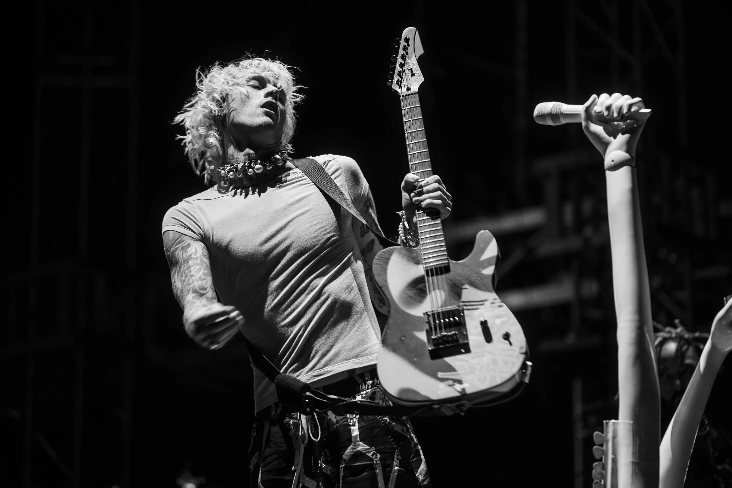 Black and white photo of a musician performing on stage, holding an electric guitar and singing into a microphone.