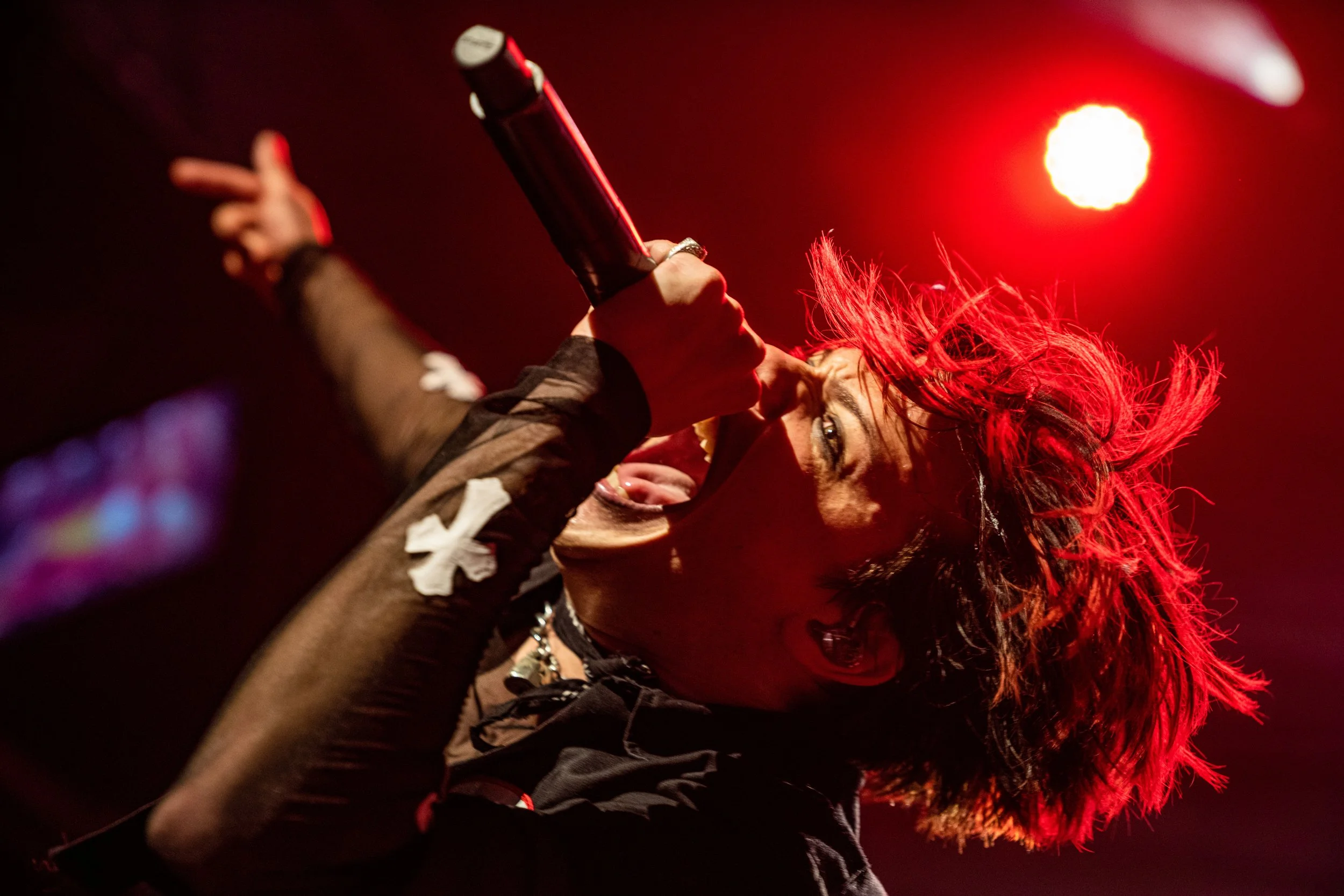 A woman with red hair singing passionately into a microphone on stage, with a red light behind her.
