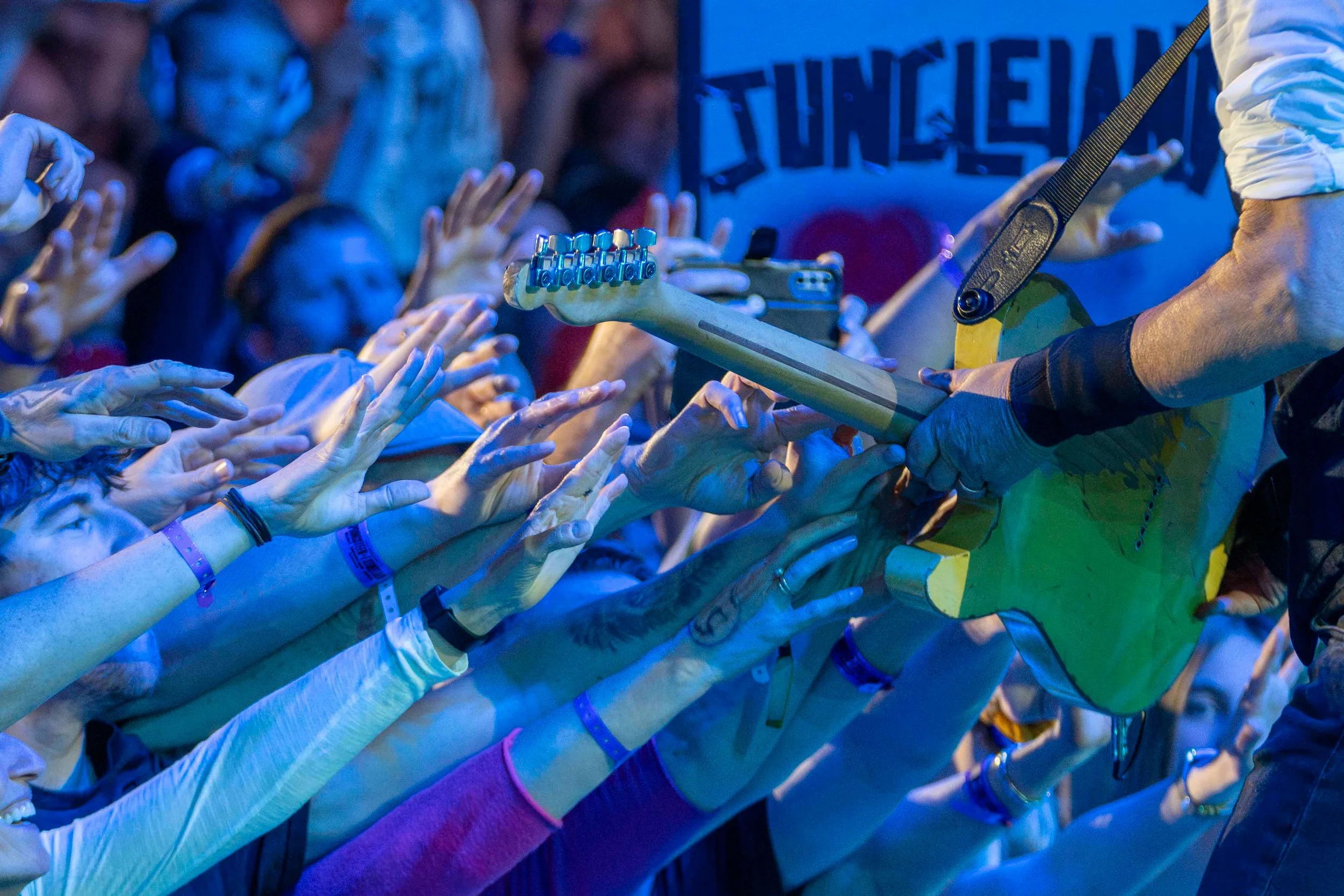 Musicians performing on stage at a concert, audience reaching out with hands and arms towards the performers.