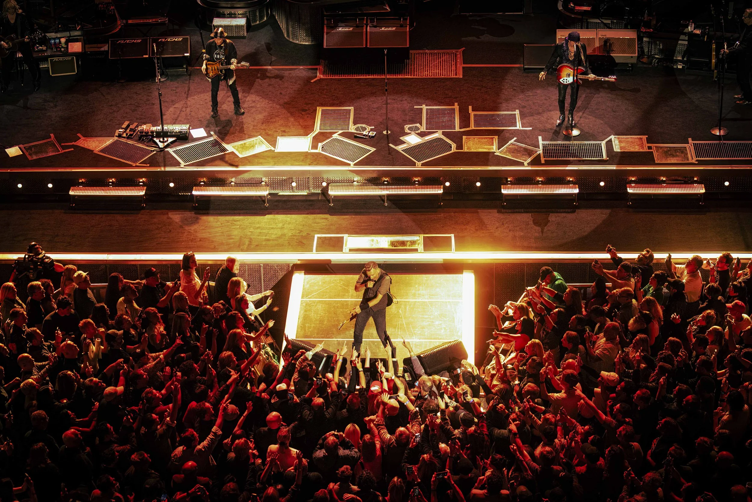 Musician performing on stage with crowd in front, stage lights illuminating the scene.