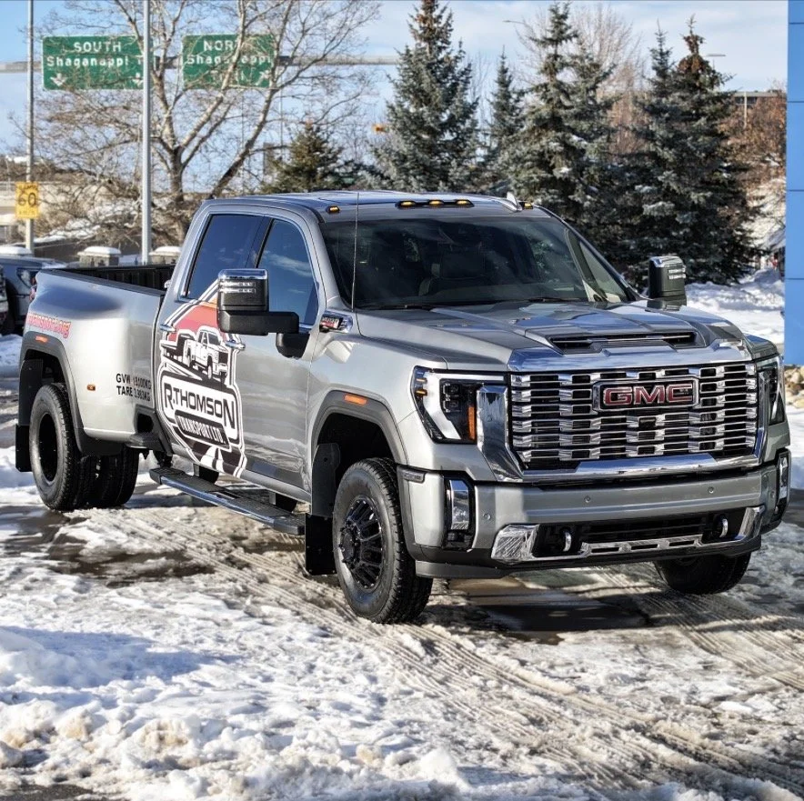 Silver GMC heavy-duty dually truck with R. Thomson Transport branding parked in Calgary, Alberta, used for hot shot trucking, flat deck hauling, and expedited freight transport services.