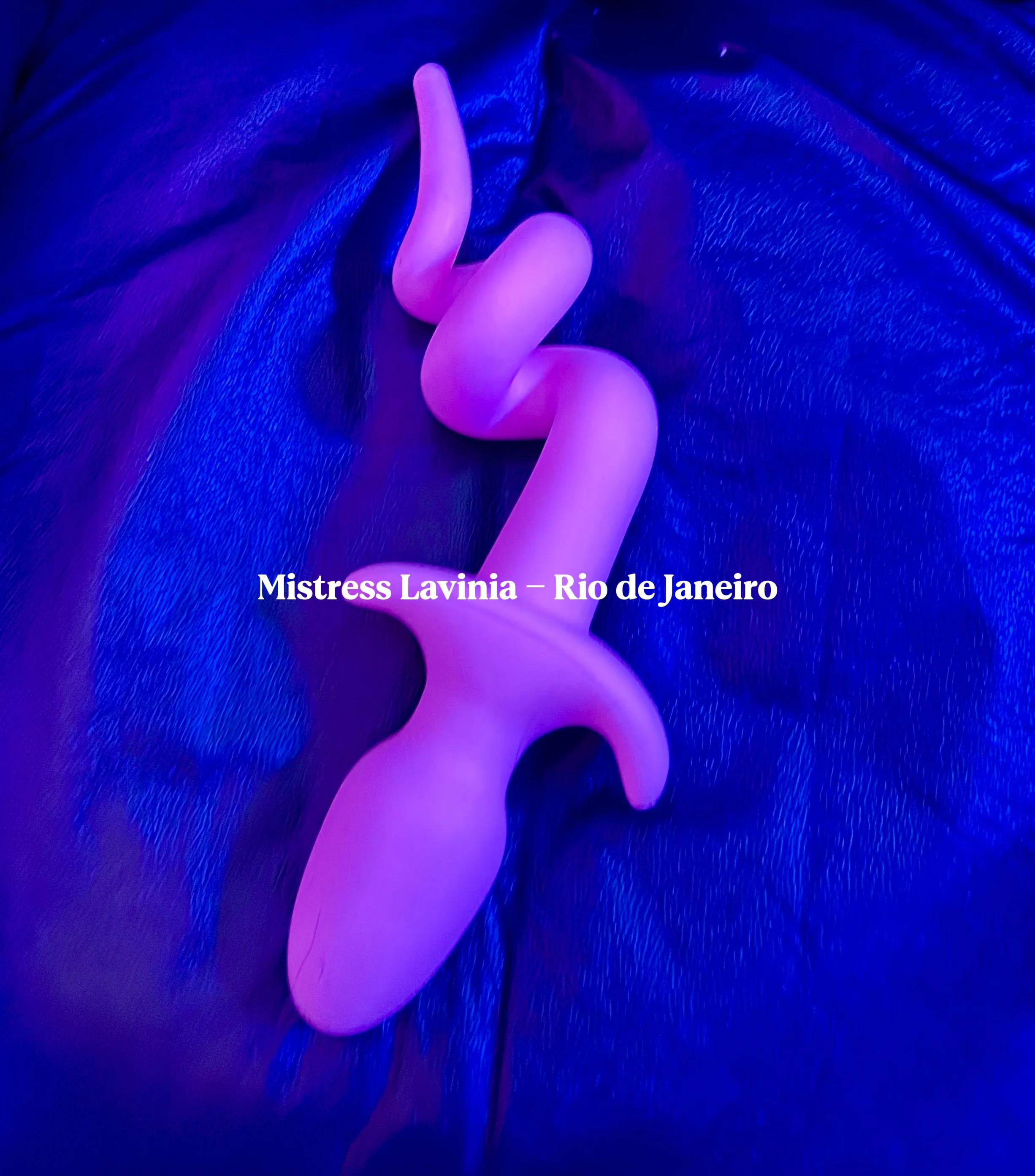 Objeto de cor rosa em formato de cobra, colocando sobre uma superfície de couro azul, com texto 'Mistress Lavinia - Rio de Janeiro'.