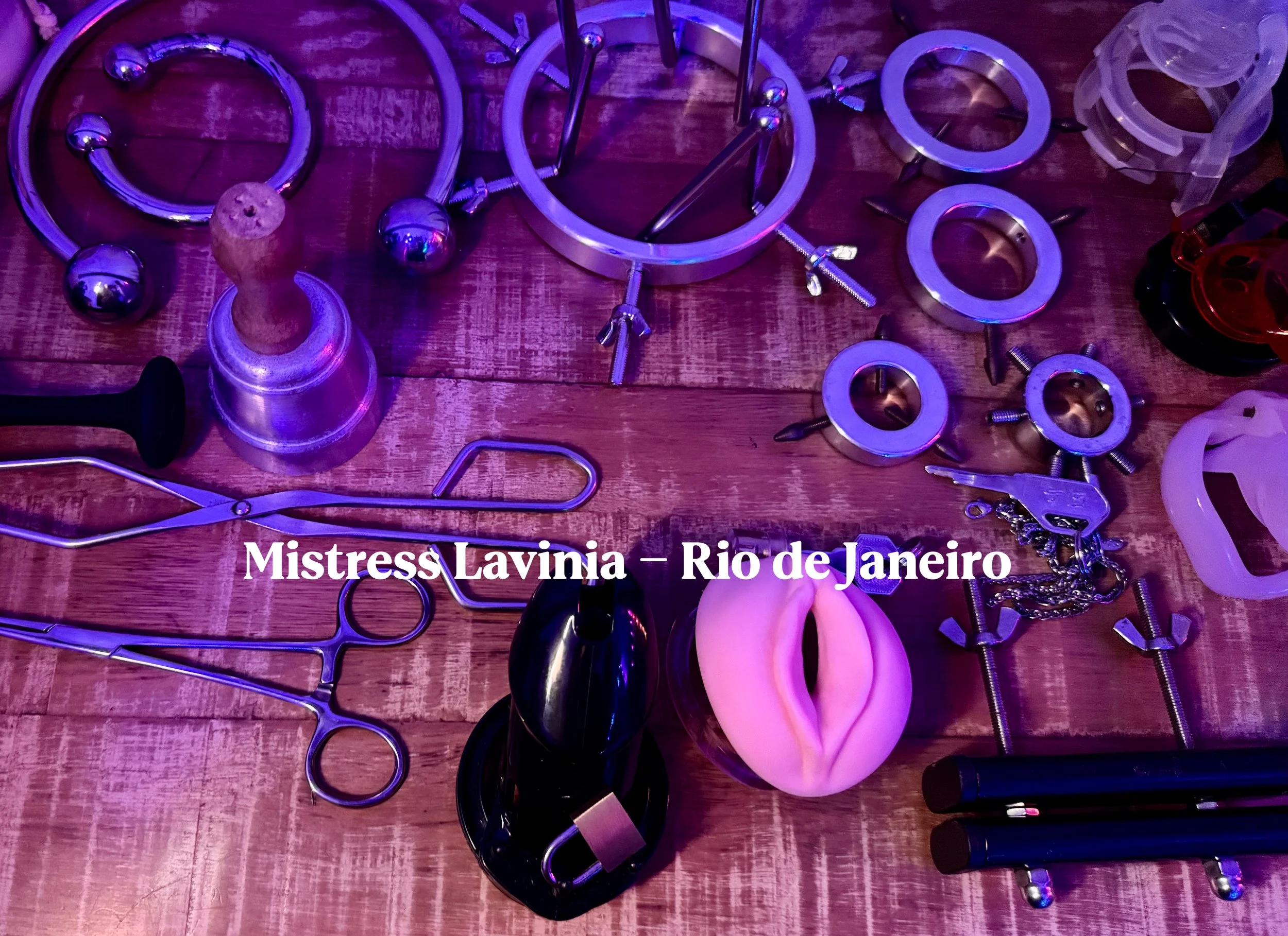 Conjunto de brinquedos e objetos de BDSM em uma mesa de madeira, incluindo algemas, chicotes, plugs anais, cordas, e outros acessórios. O texto na imagem diz "Mistress Lavinia - Rio de Janeiro".