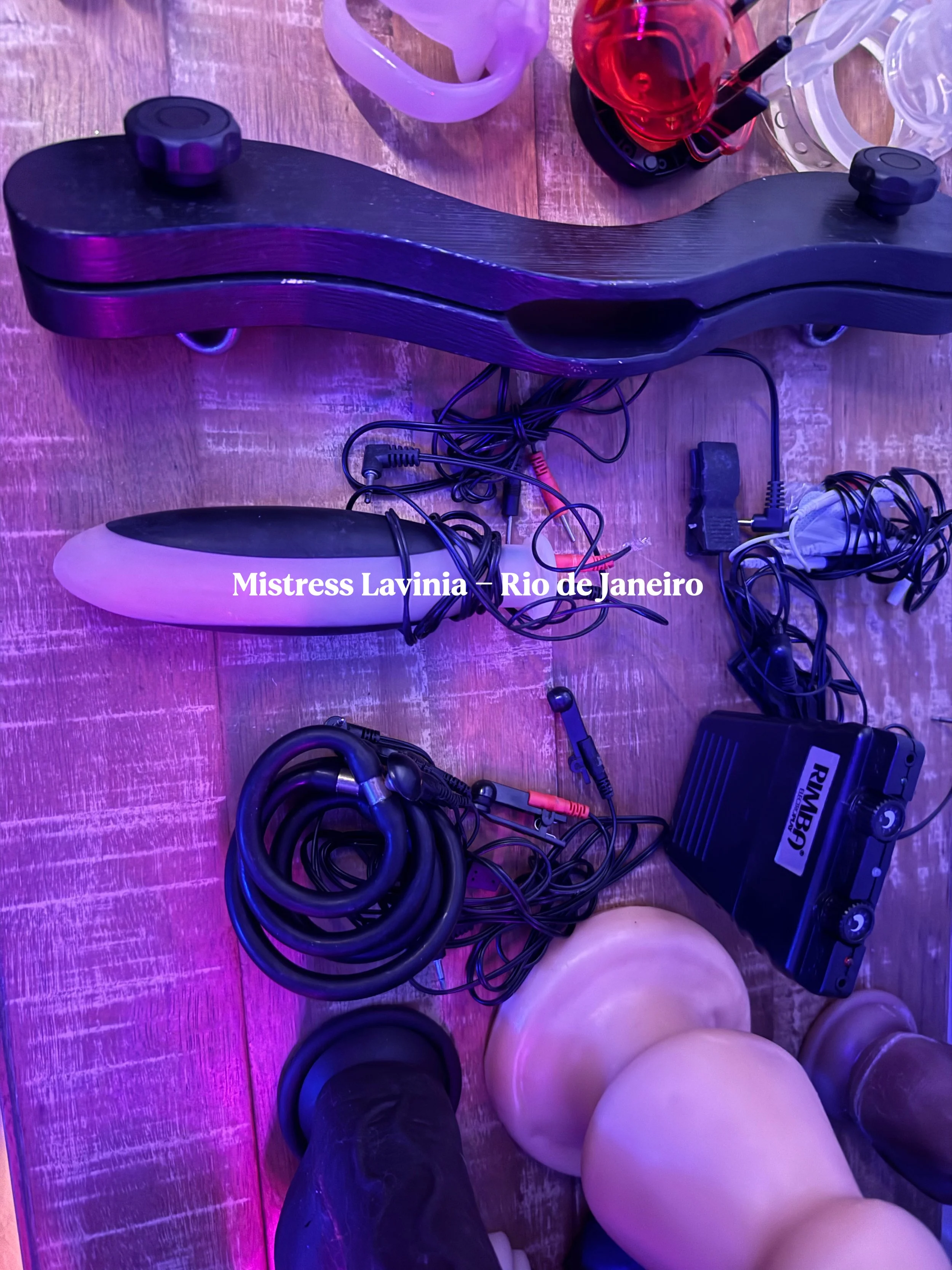 Vários equipamentos de áudio e iluminação espalhados sobre uma mesa de madeira, incluindo cabos, uma caixa de som, português e luzes de fibra óptica, sob iluminação com tom roxo.