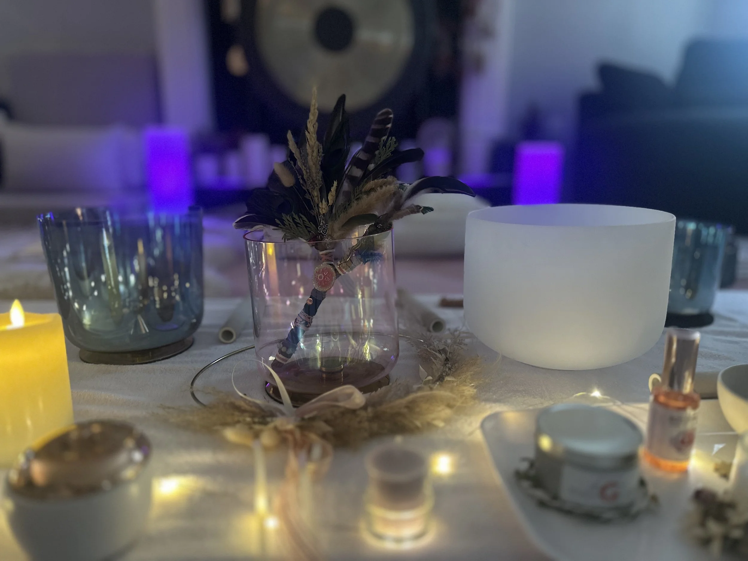 Table setting with candles, a glass vase with feathers and decorative items, and various bowls, in a softly lit room with purple and blue lighting.