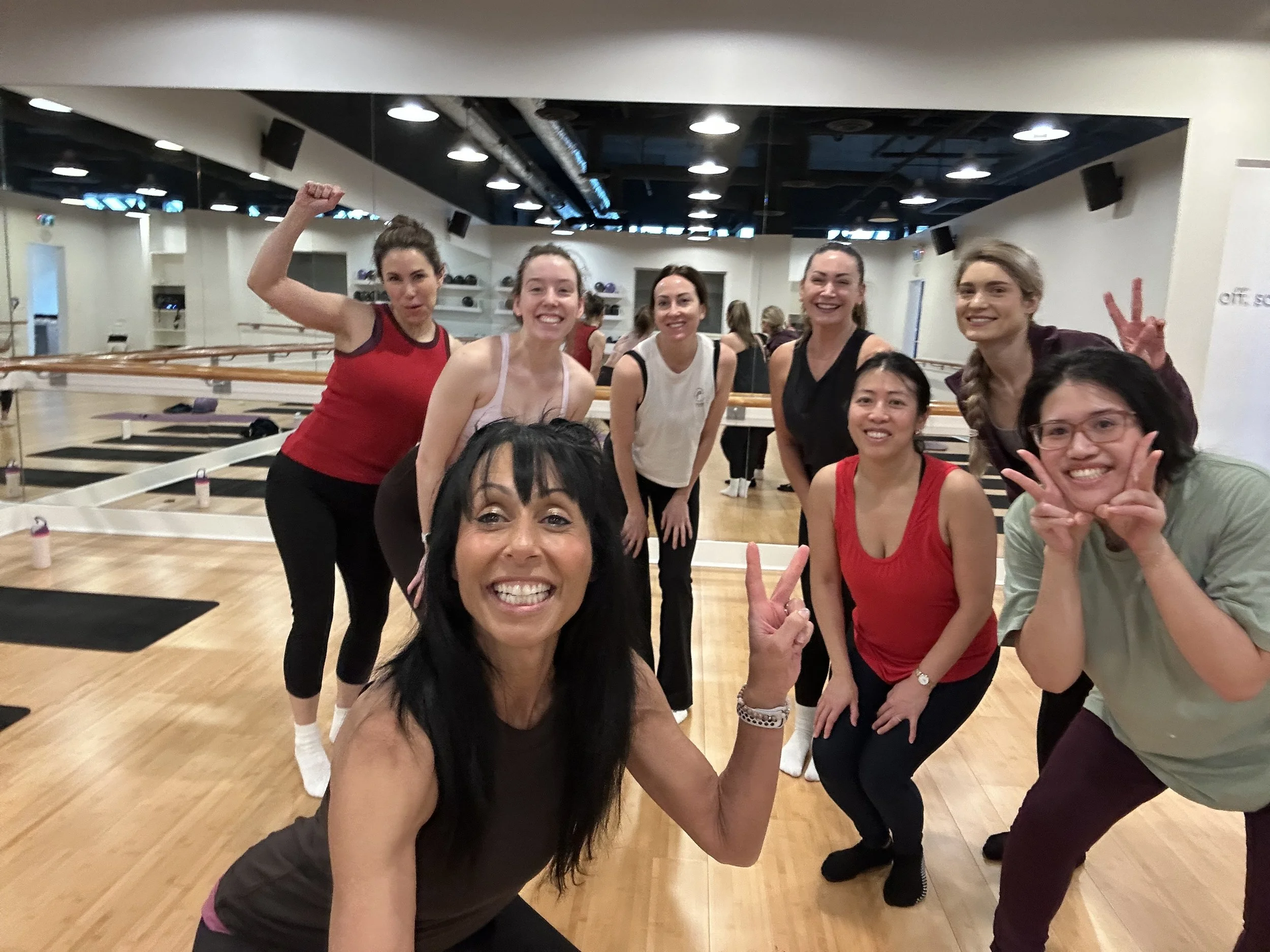 Group of women at a fitness or dance studio posing and smiling for a group photo.
