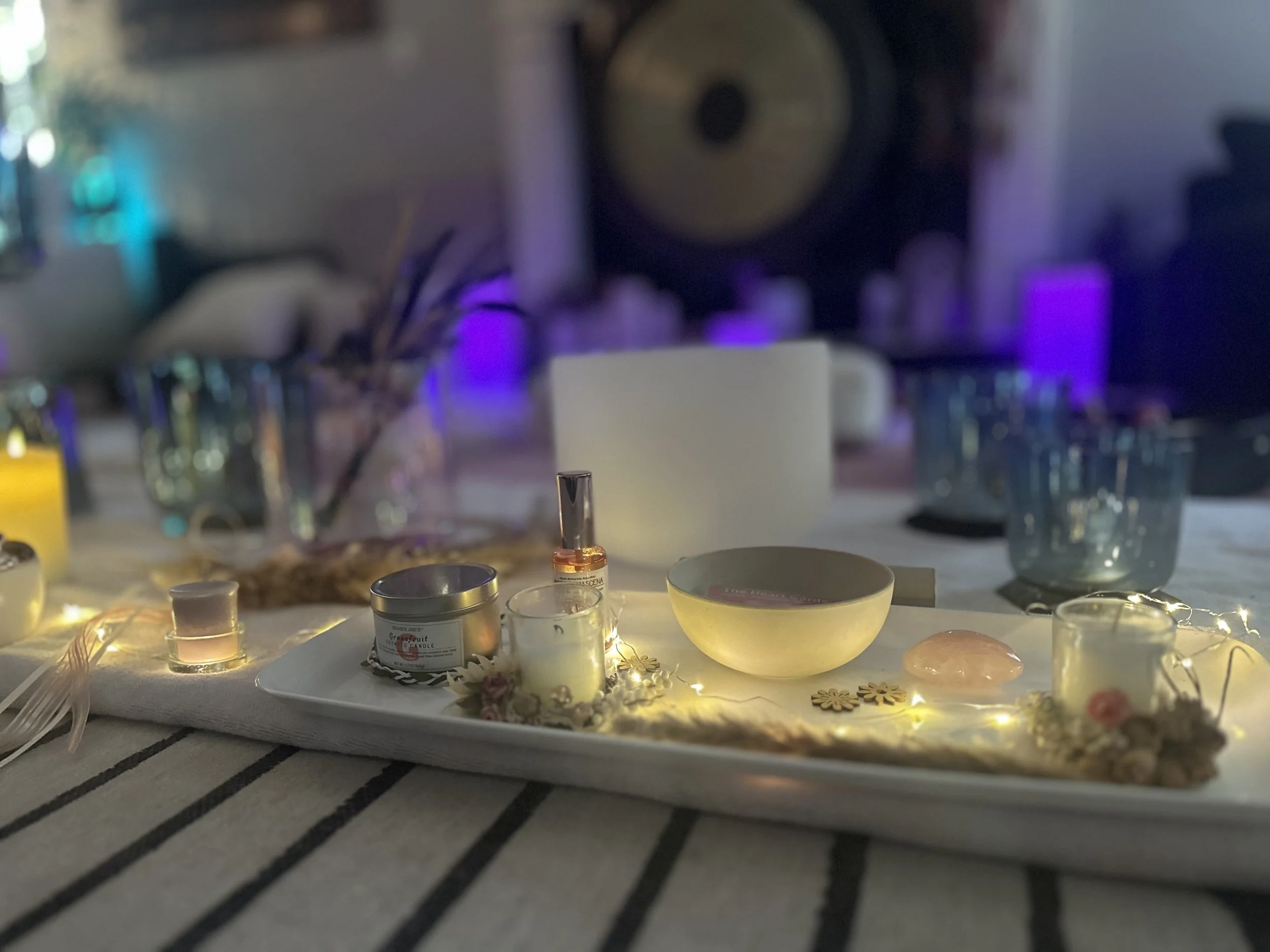 Decorative table setting with candles, small bowls, a jar, and fairy lights on a striped tablecloth, with blurred background including colorful lighting and a large speaker.