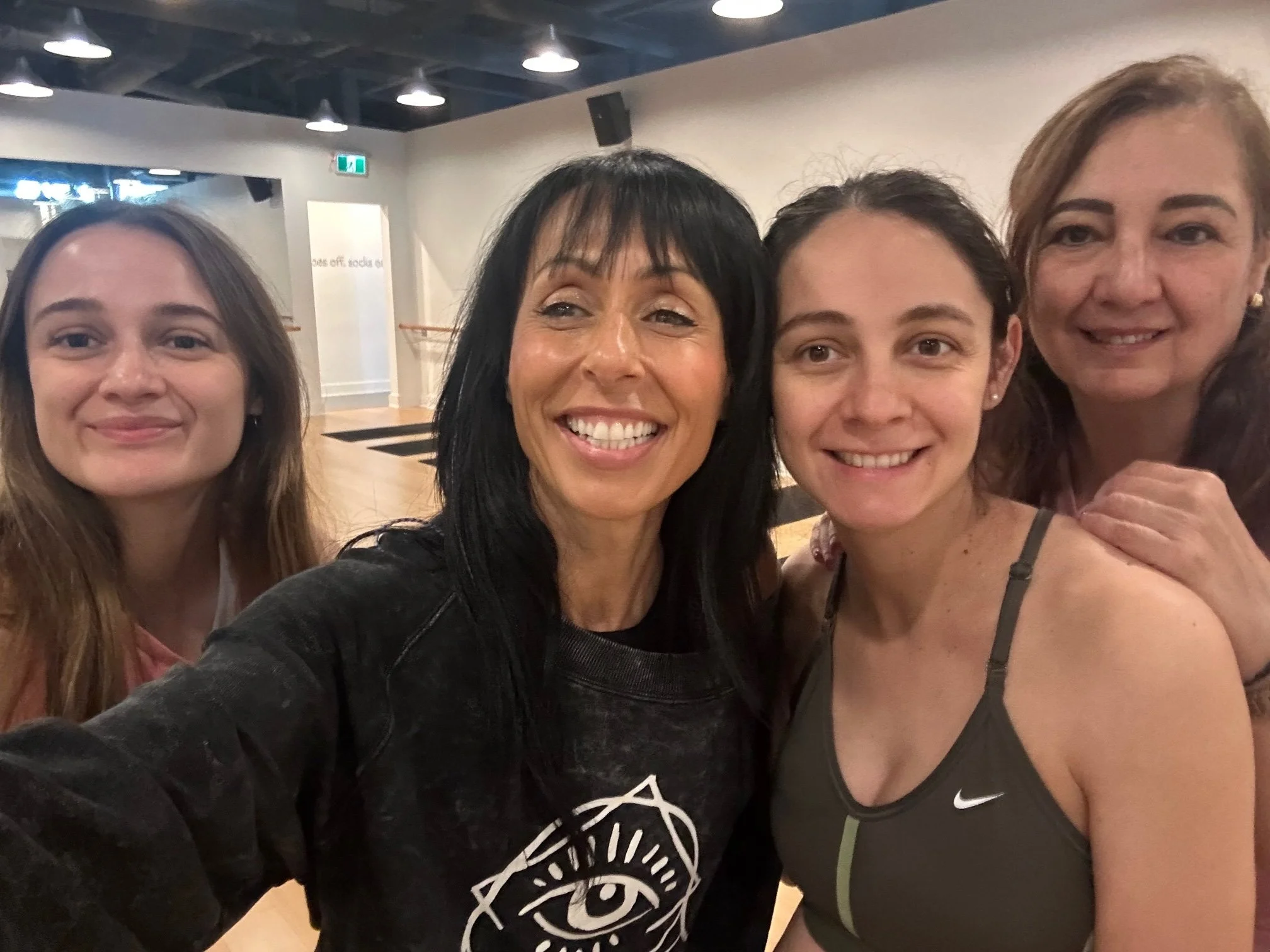Four women taking a selfie together in a gym or dance studio, smiling at the camera.