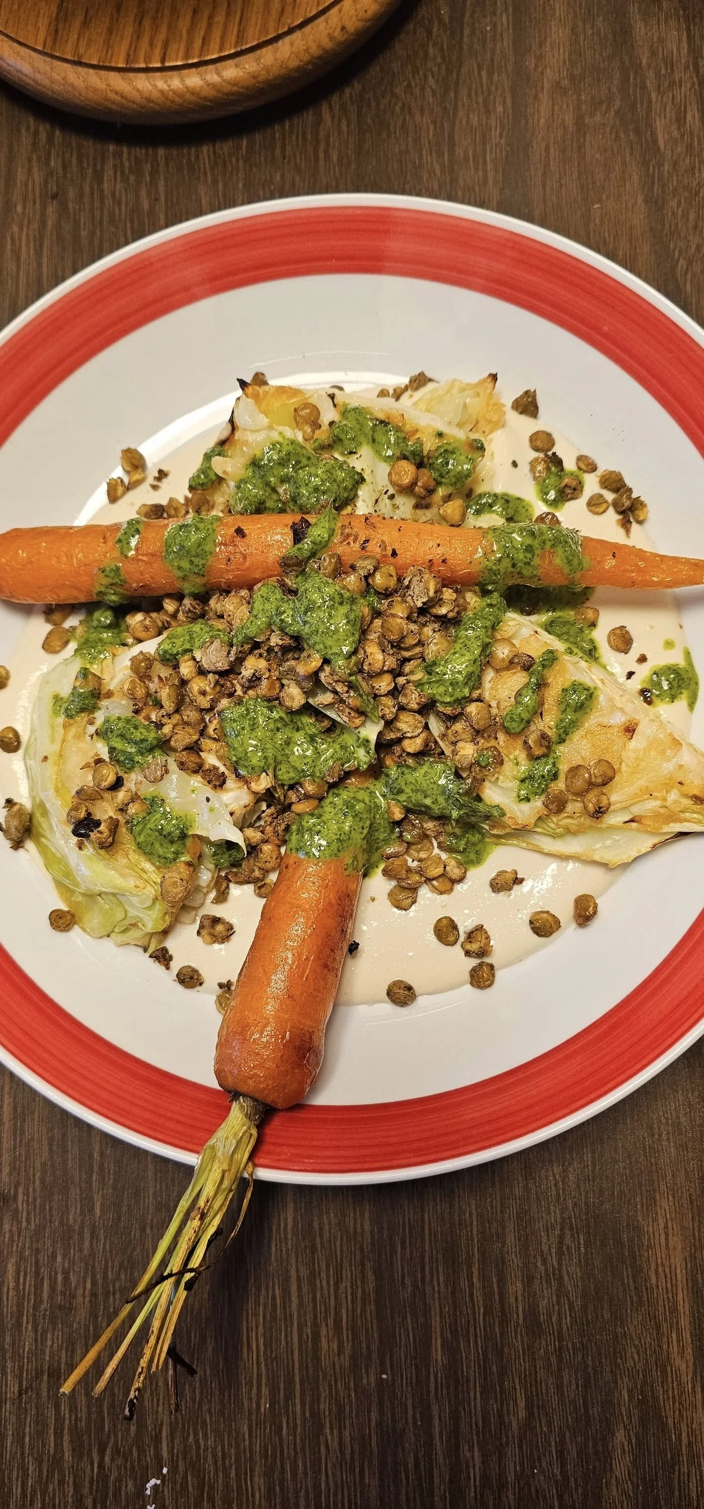 A plate of roasted vegetables including carrots, cauliflower, and kale, topped with lentils and green sauce