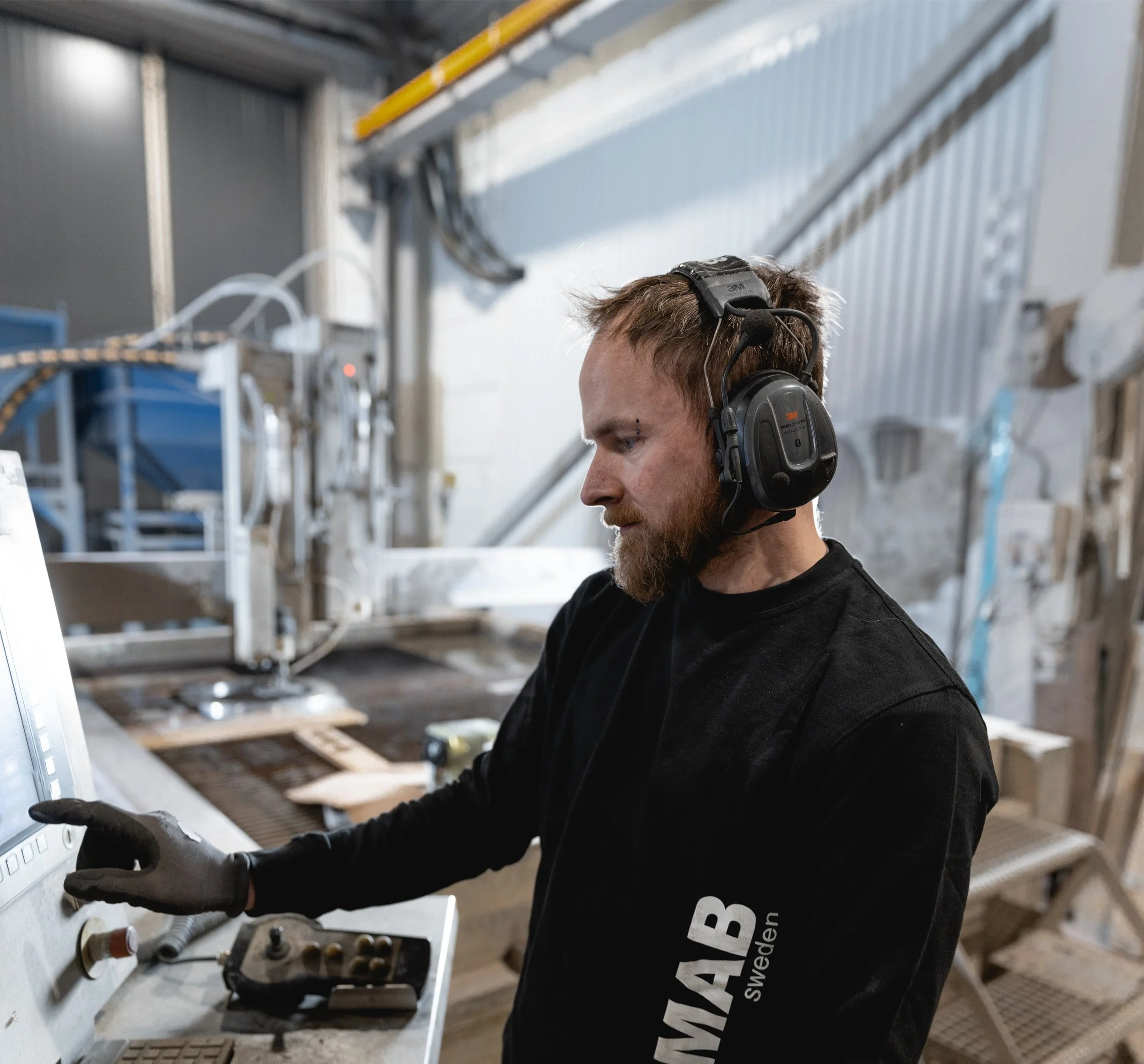 Man i skyddsutrustning arbetar med maskin i en industrilokal.