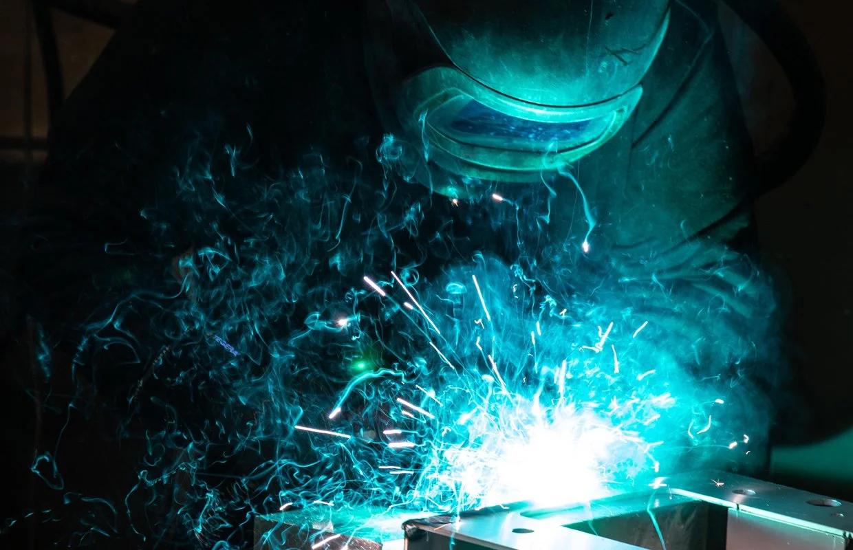 Svensk text saknas, men bilden visar en person som svetsar, med gnistor och blått ljus från svetsen.