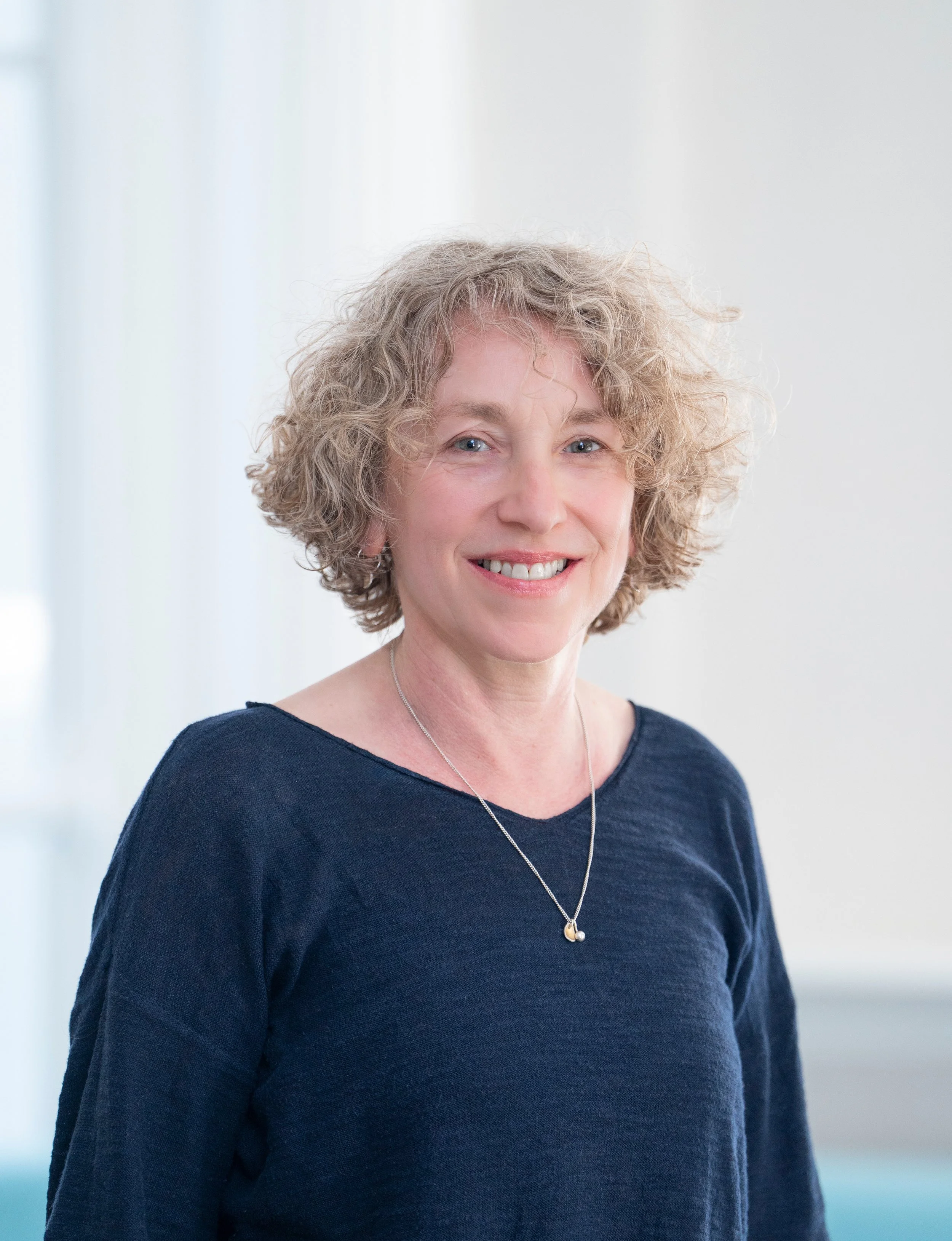 A woman with short curly blonde hair and a blue jumper.