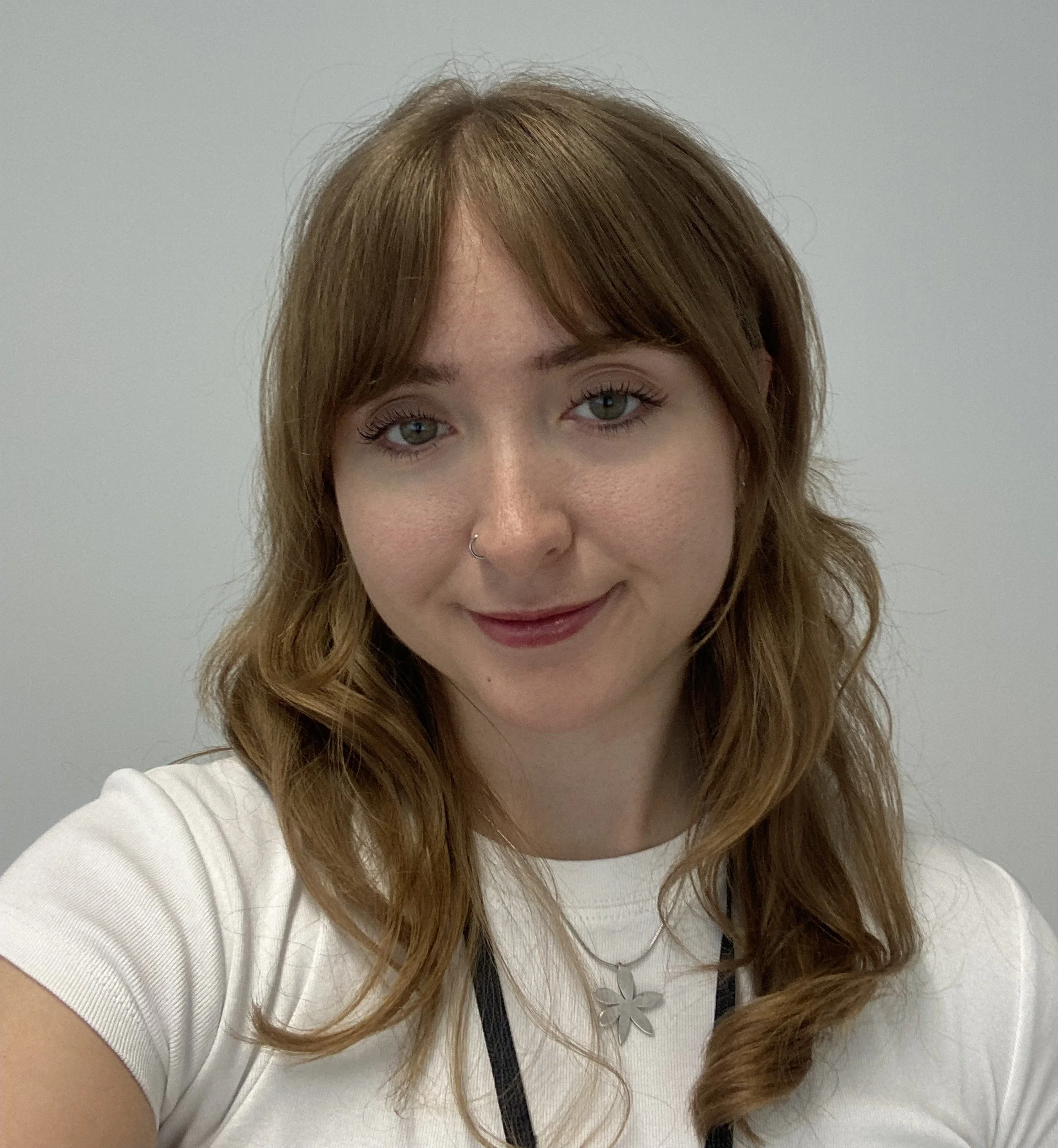 A woman with long auburn hair and a white t shirt. She is smiling at the camera.