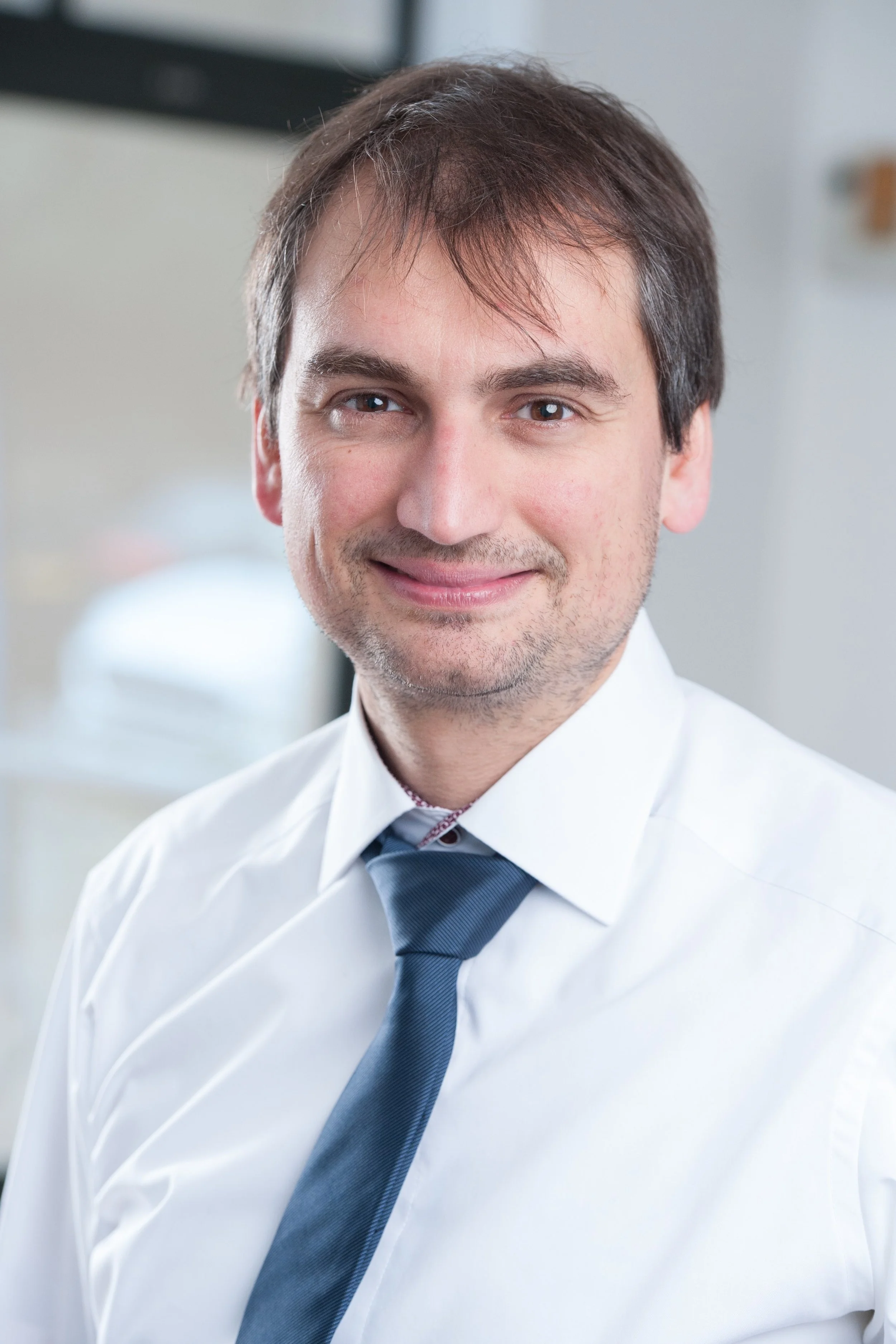 Man wearing a white shirt and blue tie smiling at the camera.