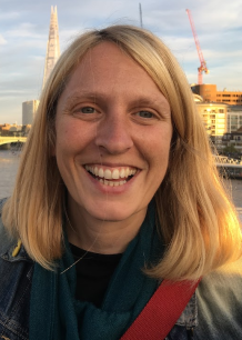 Close-up of a smiling woman with blonde hair, city skyline and river in the background, during sunset.