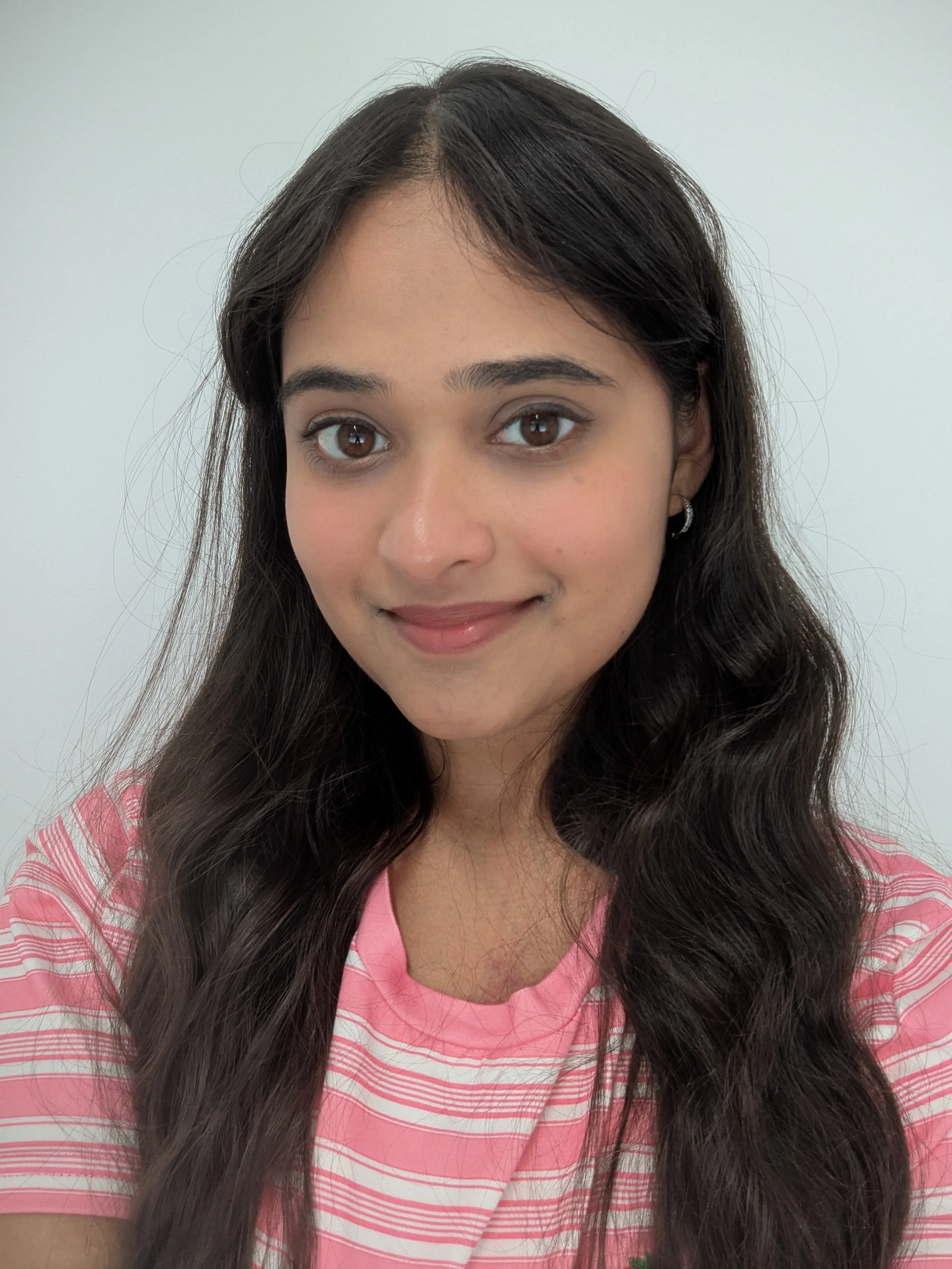 A woman with long dark brown hair and a pink stripy t-shirt on. She is smiling at the camera.