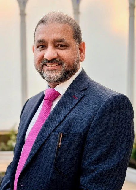 Man wearing a blue blazer and pink tie smiling at the camera.