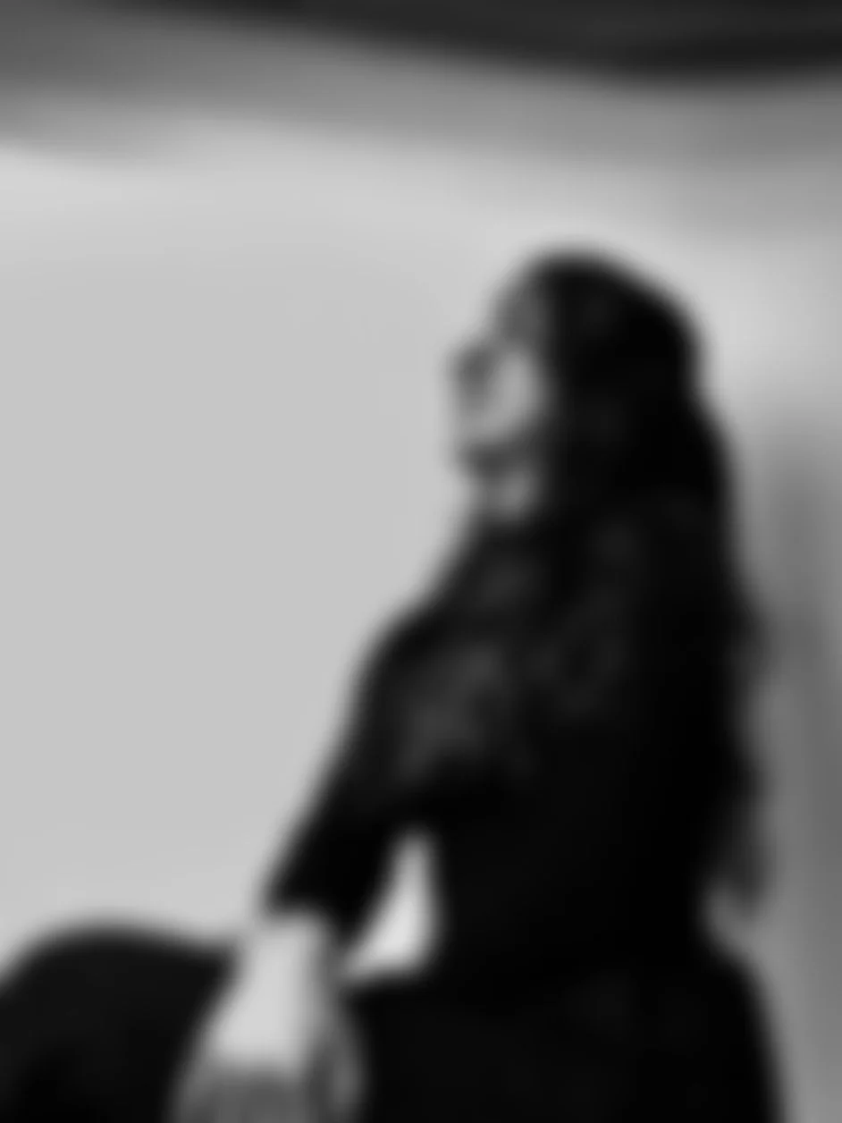 Blurry black and white photo of a woman with long hair, sitting with crossed arms and smiling, against a plain background.