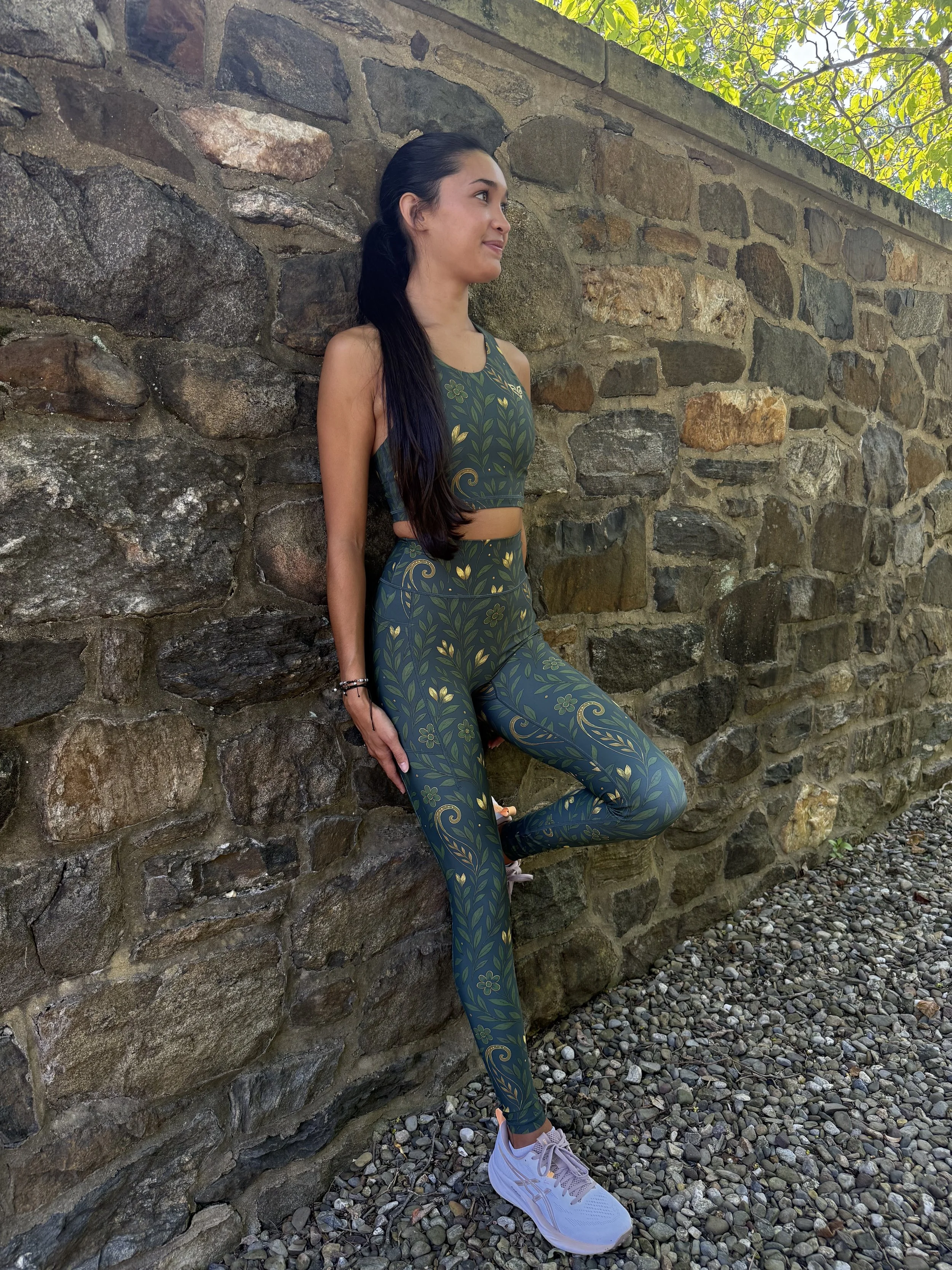 Woman wearing an Eryvalen patterned running set while leaning against a stone wall outdoors.