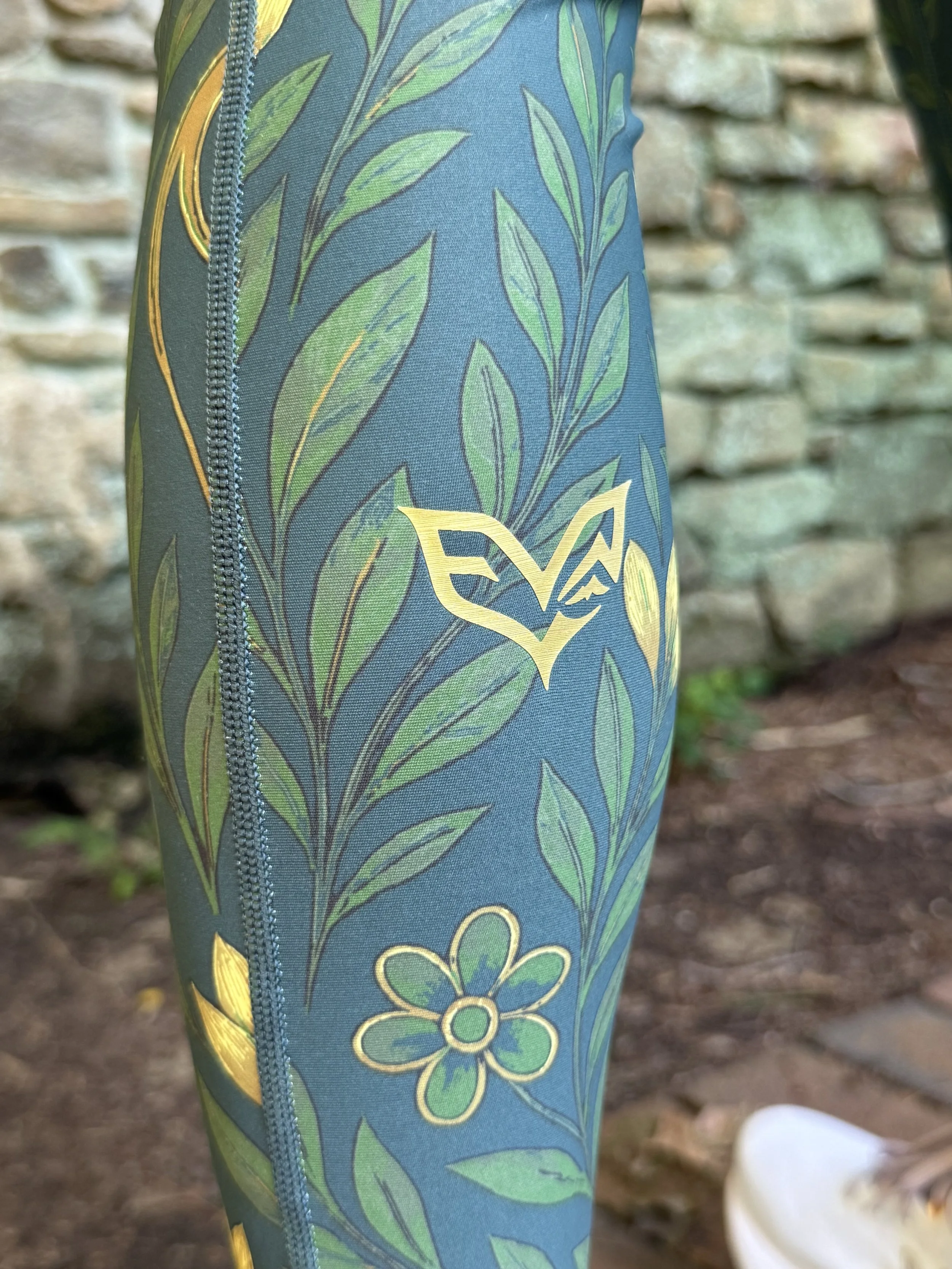 Close-up of Eryvalen green floral performance leggings with gold logo and side pocket.