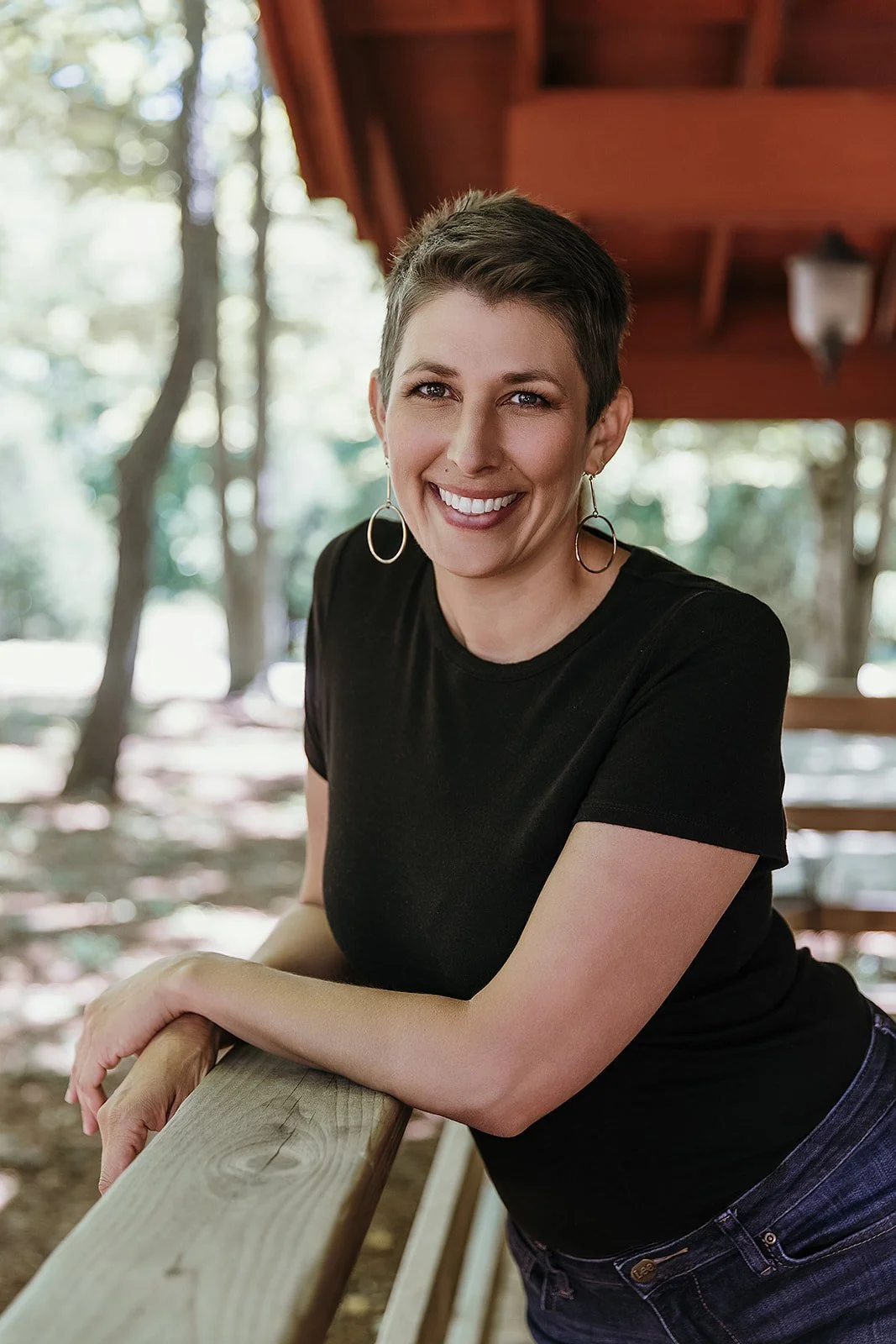 Liza Annette, therapist, smiling in a black t-shirt, leaning on a railing at a cabin in the woods