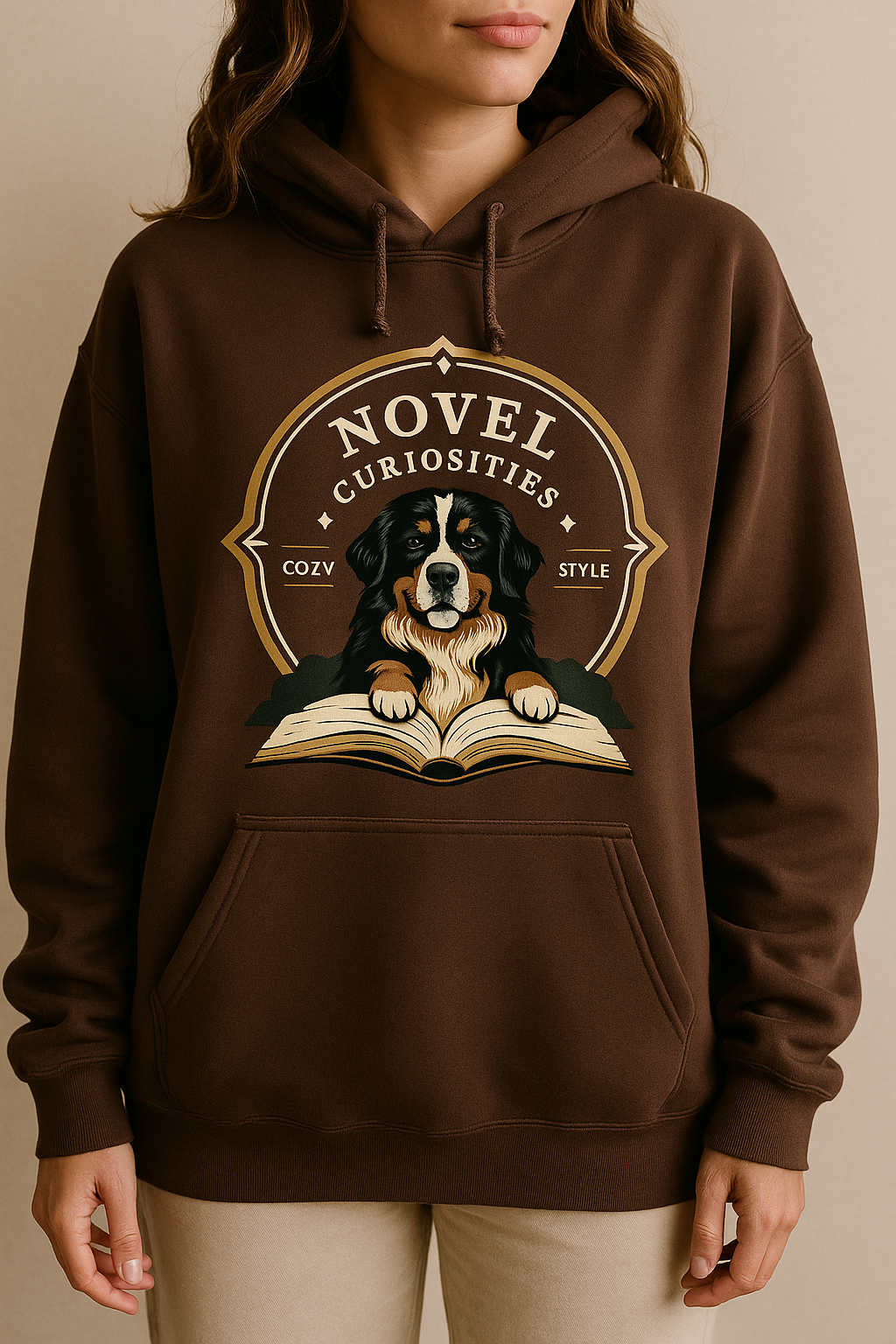 A person wearing a brown hoodie with a graphic of a dog and an open book on the front. The graphic includes the words 'Novel Curiosities' and decorative elements.