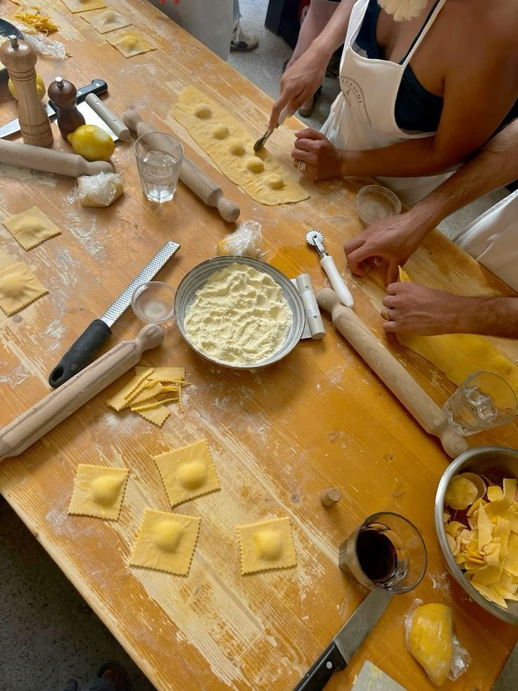 Preparazione di pasta ripiena con vari strumenti da cucina e sfoglie di pasta su un tavolo di legno.