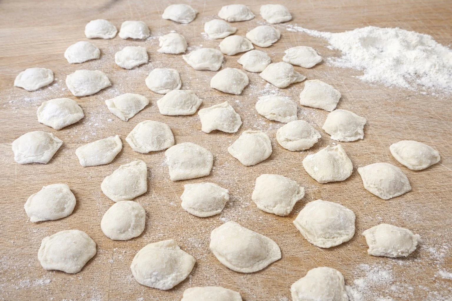 Tri file di gnocchi di patate fatti a mano su un tavolo di legno, con farina sparsa.