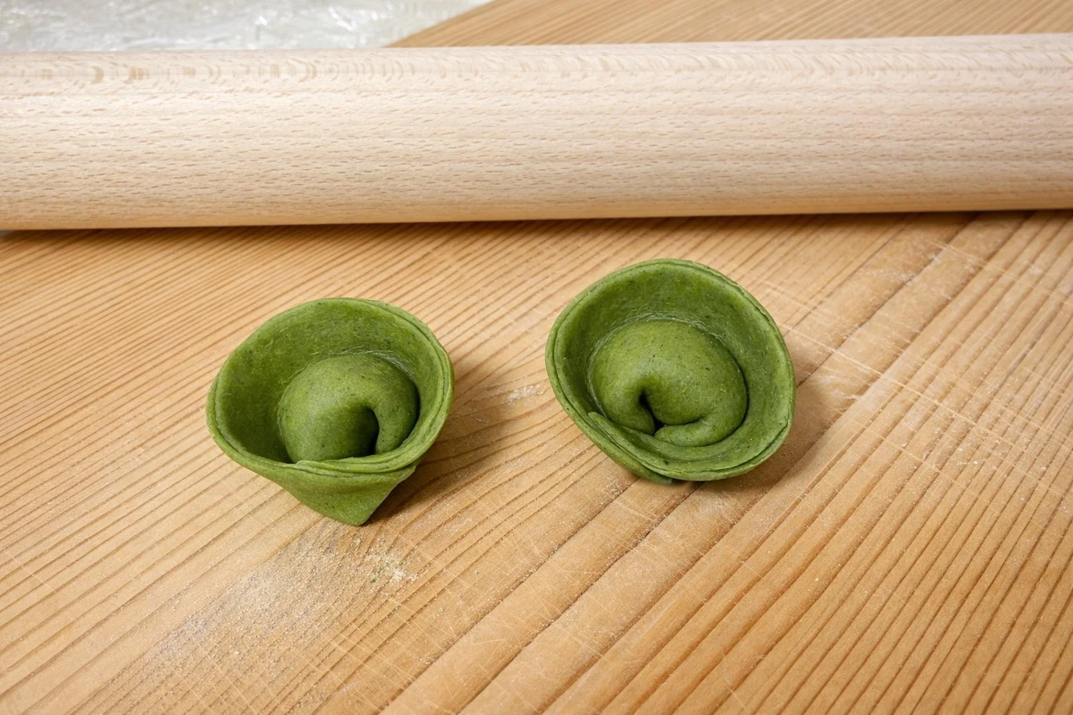 Due sfoglie di pasta verde fresca arrotolate su un piano di legno.