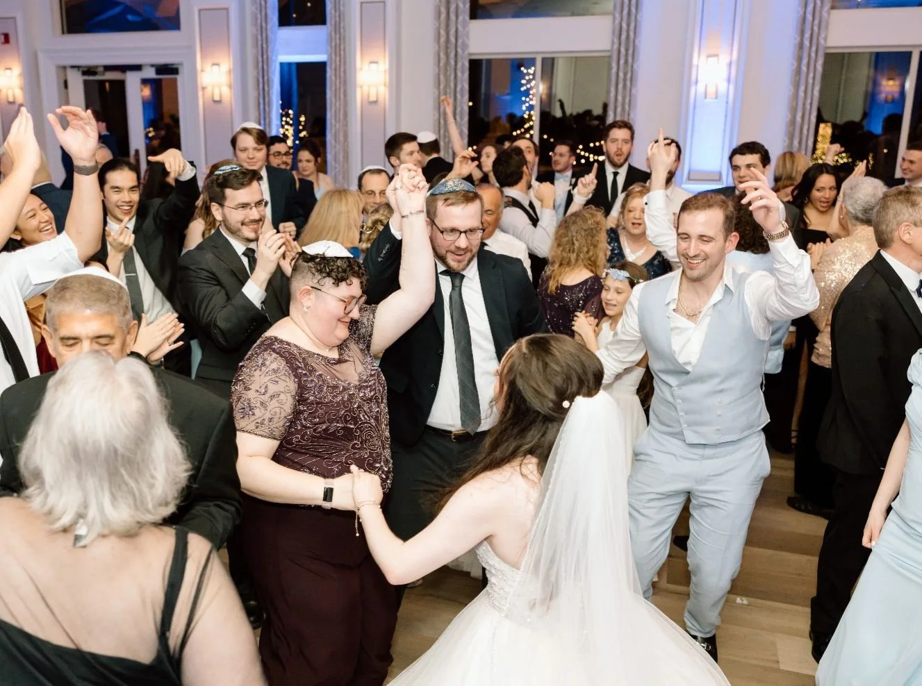 People dancing and celebrating at a wedding reception, with a bride in a white dress and veil in the foreground.