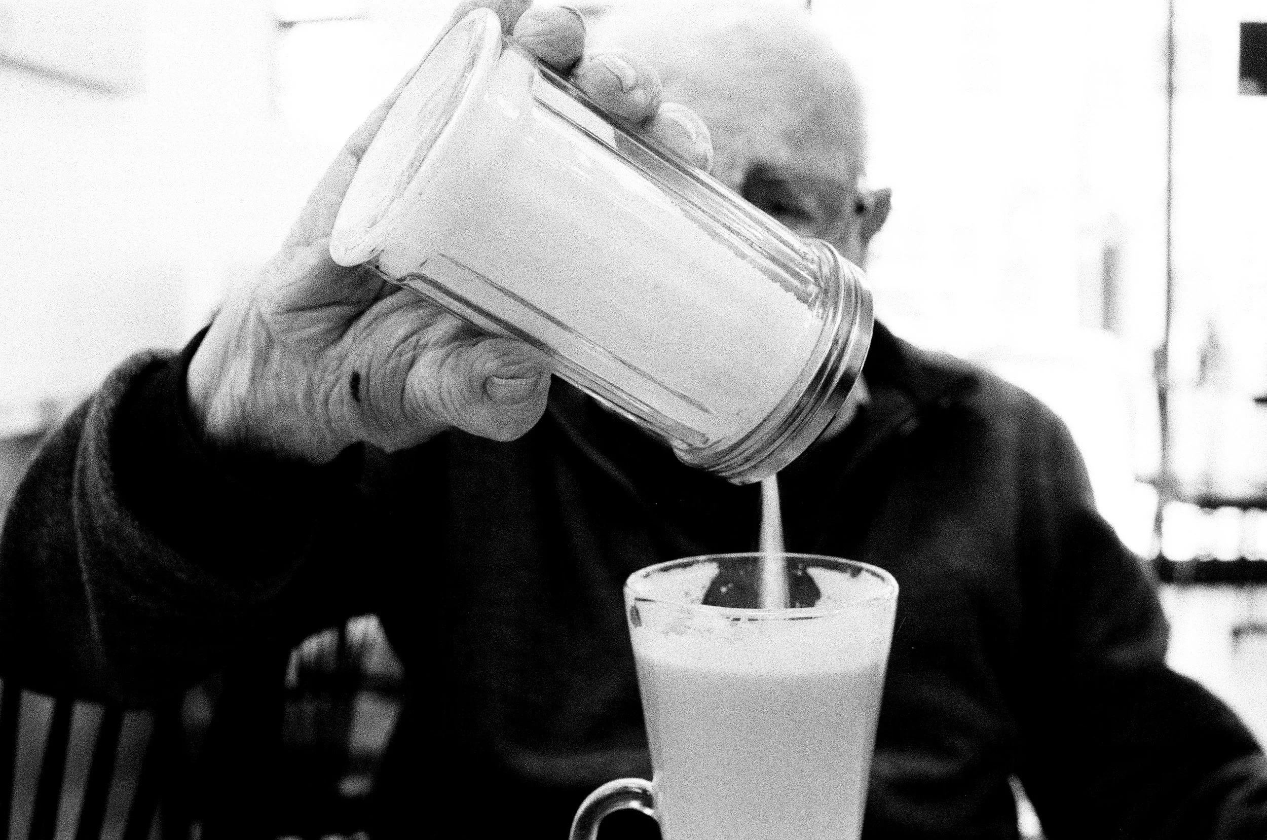 A person pouring a beverage into a glass, with a hand holding a container, in black and white.