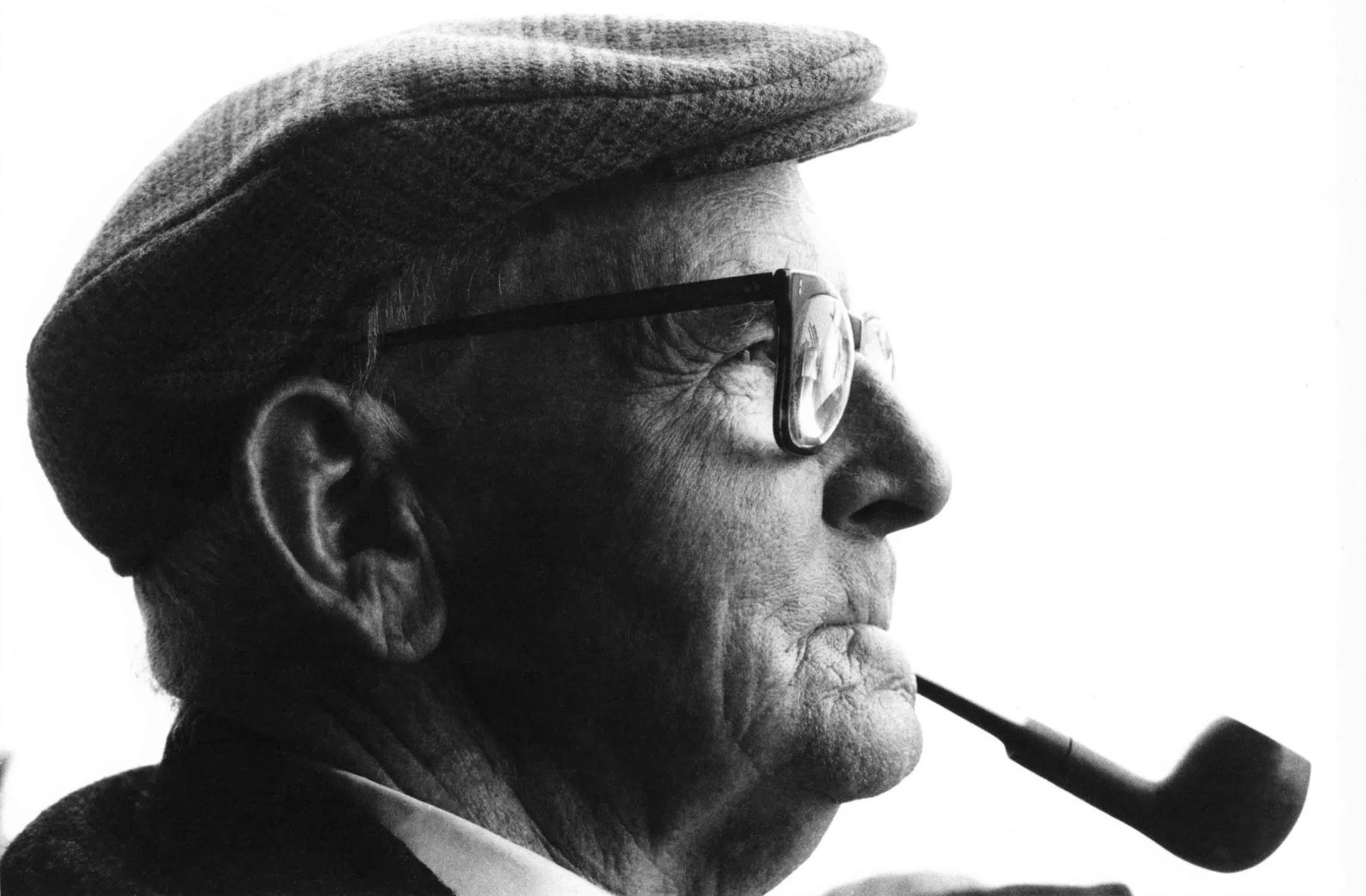 Close-up side profile of an elderly man wearing a hat and glasses, smoking a pipe in black and white.