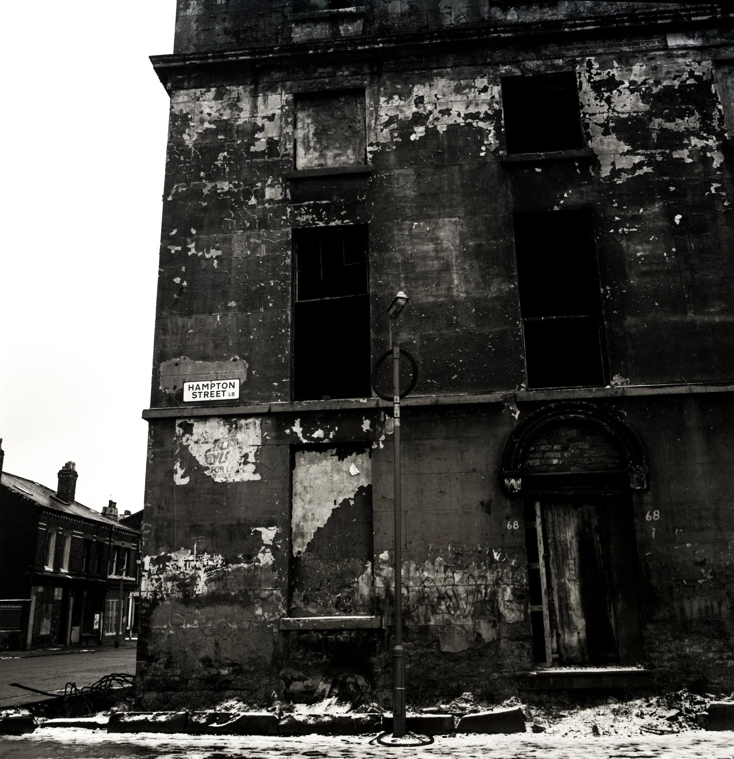 An old, abandoned building with peeling paint and boarded-up windows, located on Hampton Street, with a streetlamp in front and neighboring buildings visible in the background.